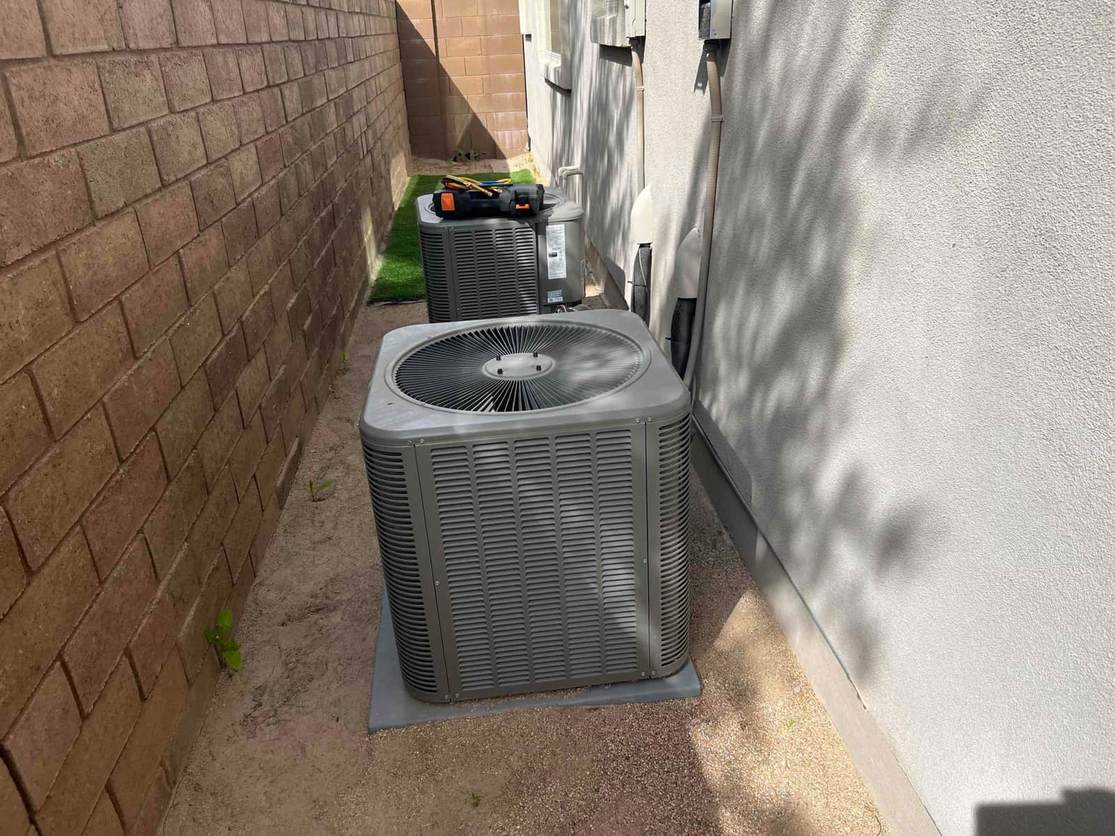 Two outdoor condenser units beside a house with disconnects and refrigerant lines visible.