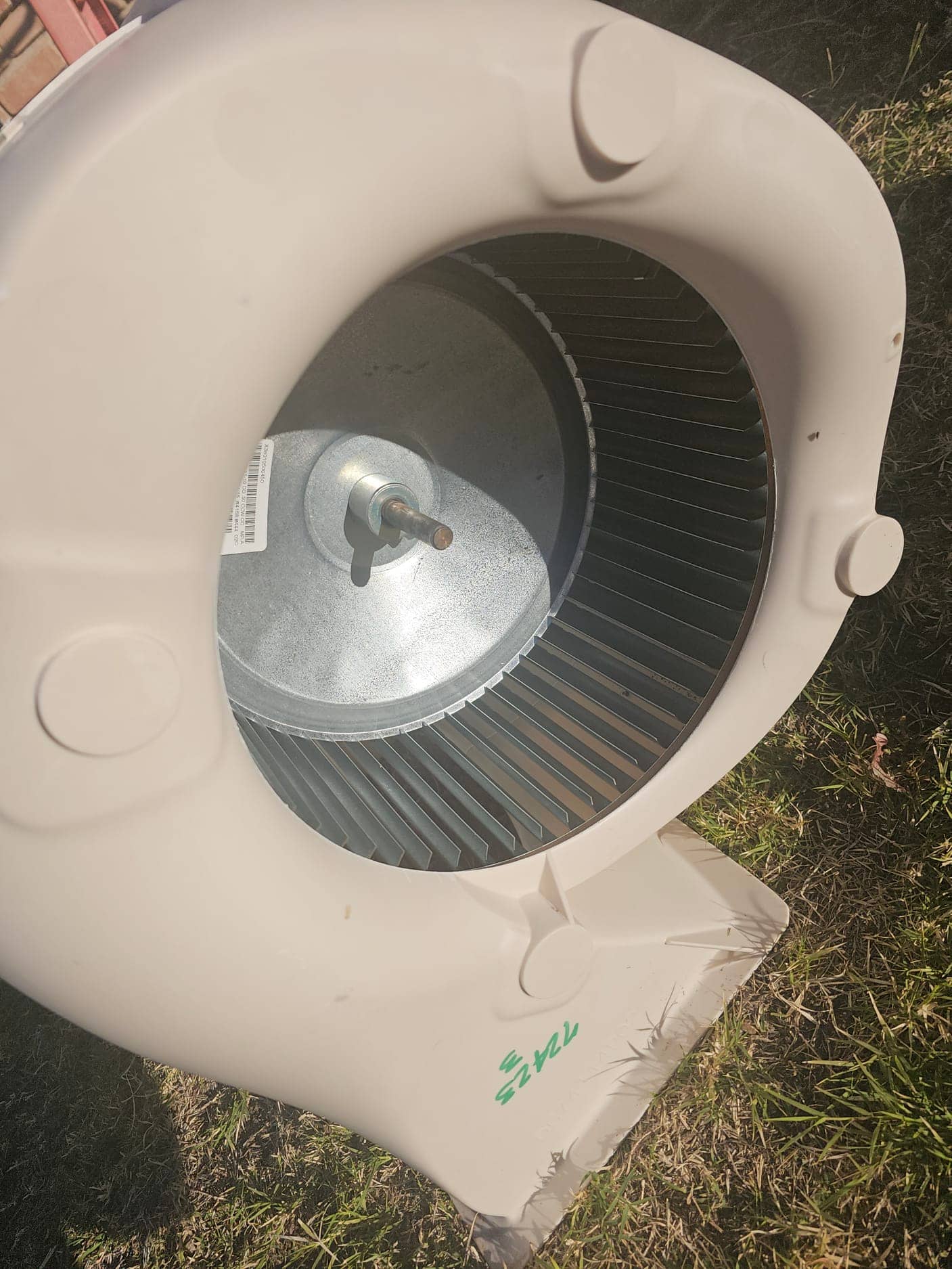 Plastic blower housing with metal squirrel-cage wheel and central shaft, positioned outdoors on grass.