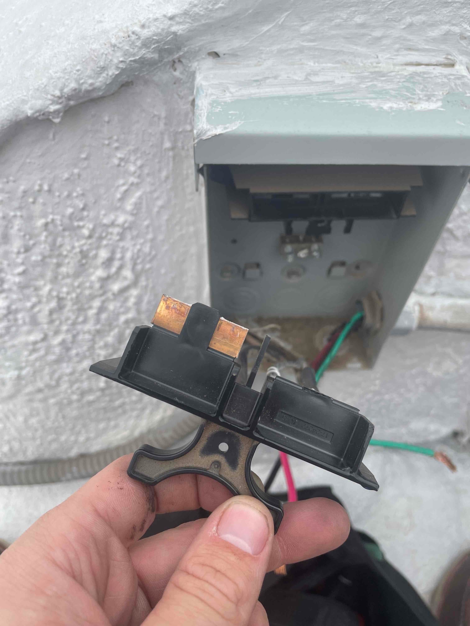 Pull-out electrical disconnect handle with copper blades, shown in front of open outdoor service disconnect with exposed wiring.