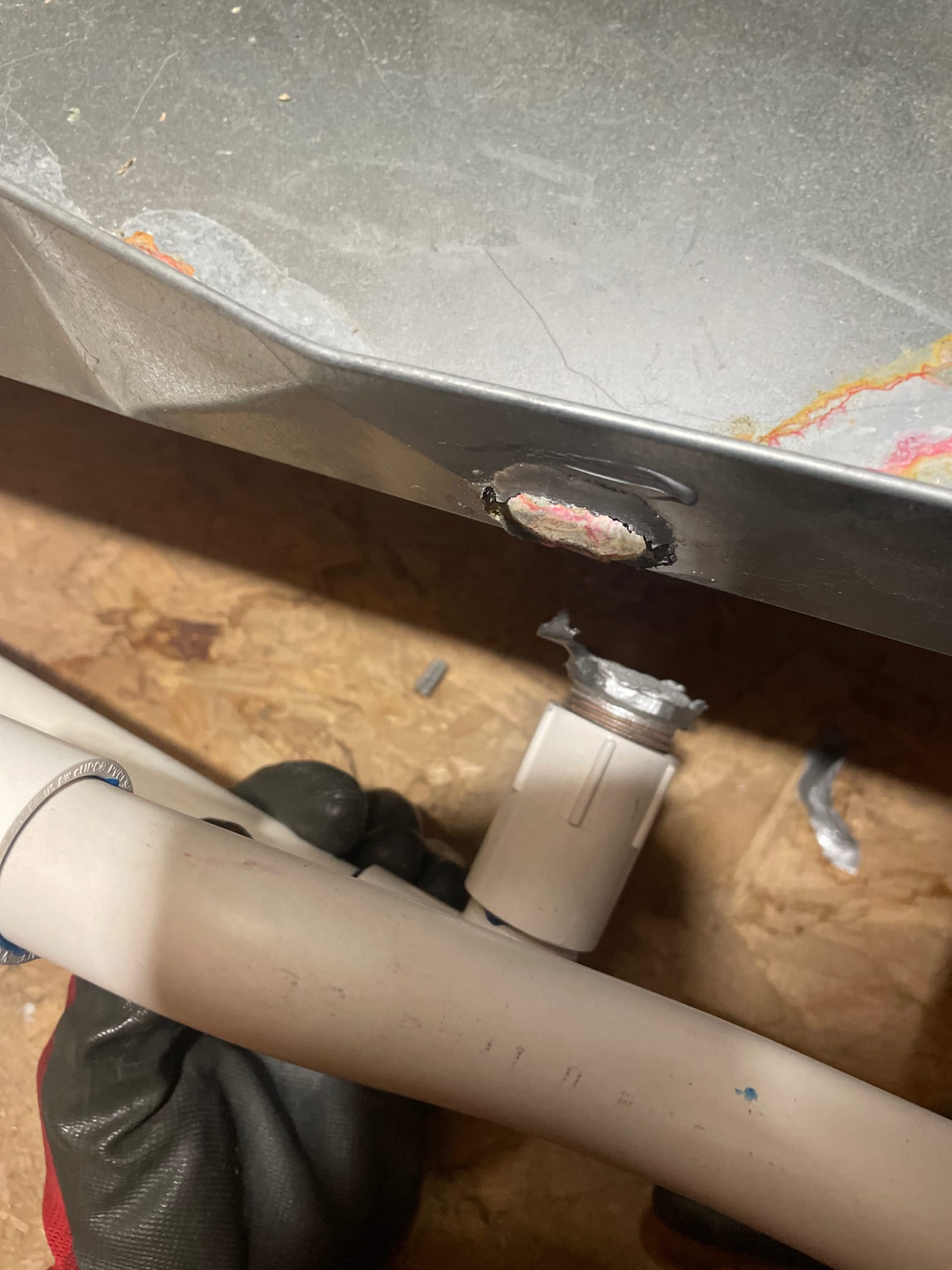 PVC drain line and threaded adapter at a metal pan, with sealant and discoloration around the opening.