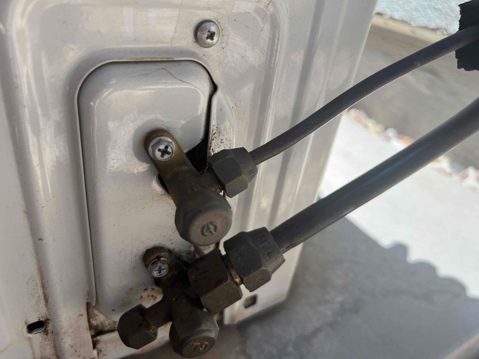 Two refrigerant line flare connections at an outdoor unit panel, with hex flare nuts and attached insulated tubing.
