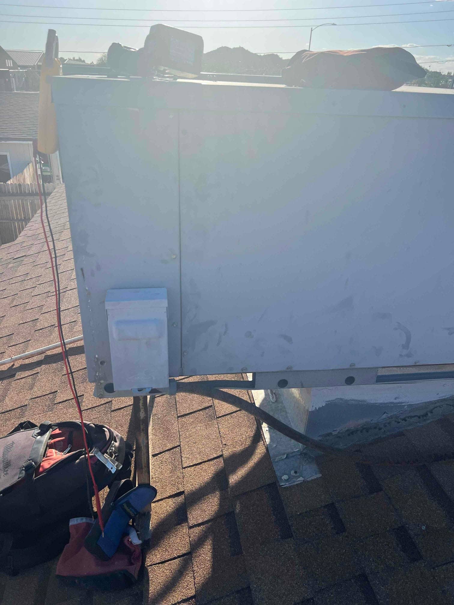 Rooftop HVAC package unit on shingle roof with exterior panel and nearby tools and leads.