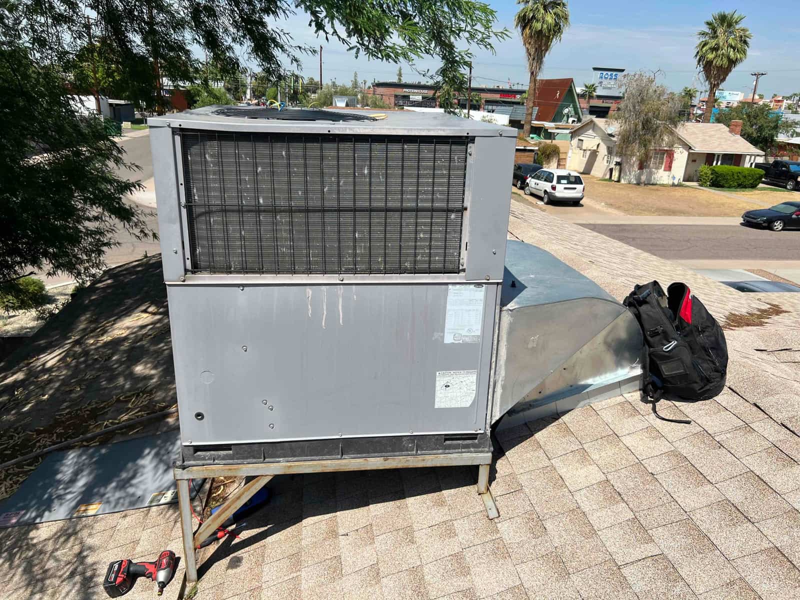 Rooftop packaged HVAC unit with coil face and attached sheet-metal duct transition on shingles.