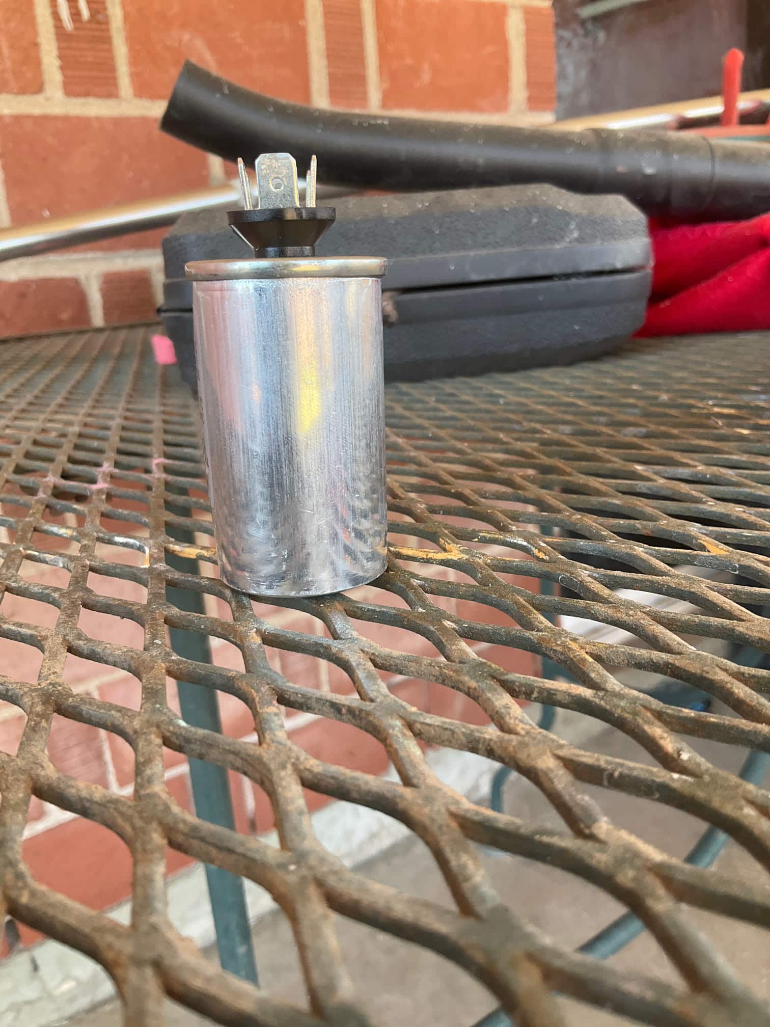 Round metal capacitor with spade terminals at the top, set on a work surface outdoors.