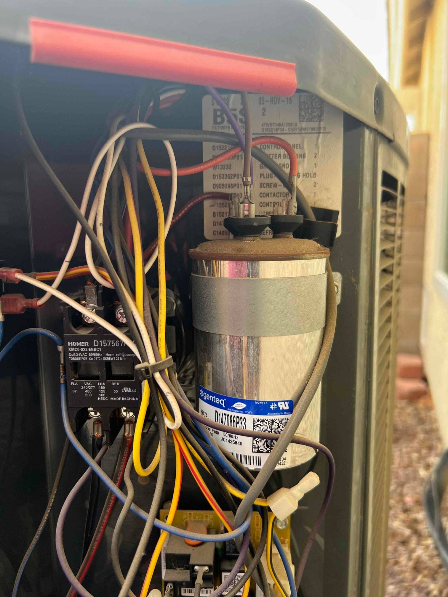 Run capacitor with multiple wires connected beside the contactor inside the outdoor condenser’s control compartment.