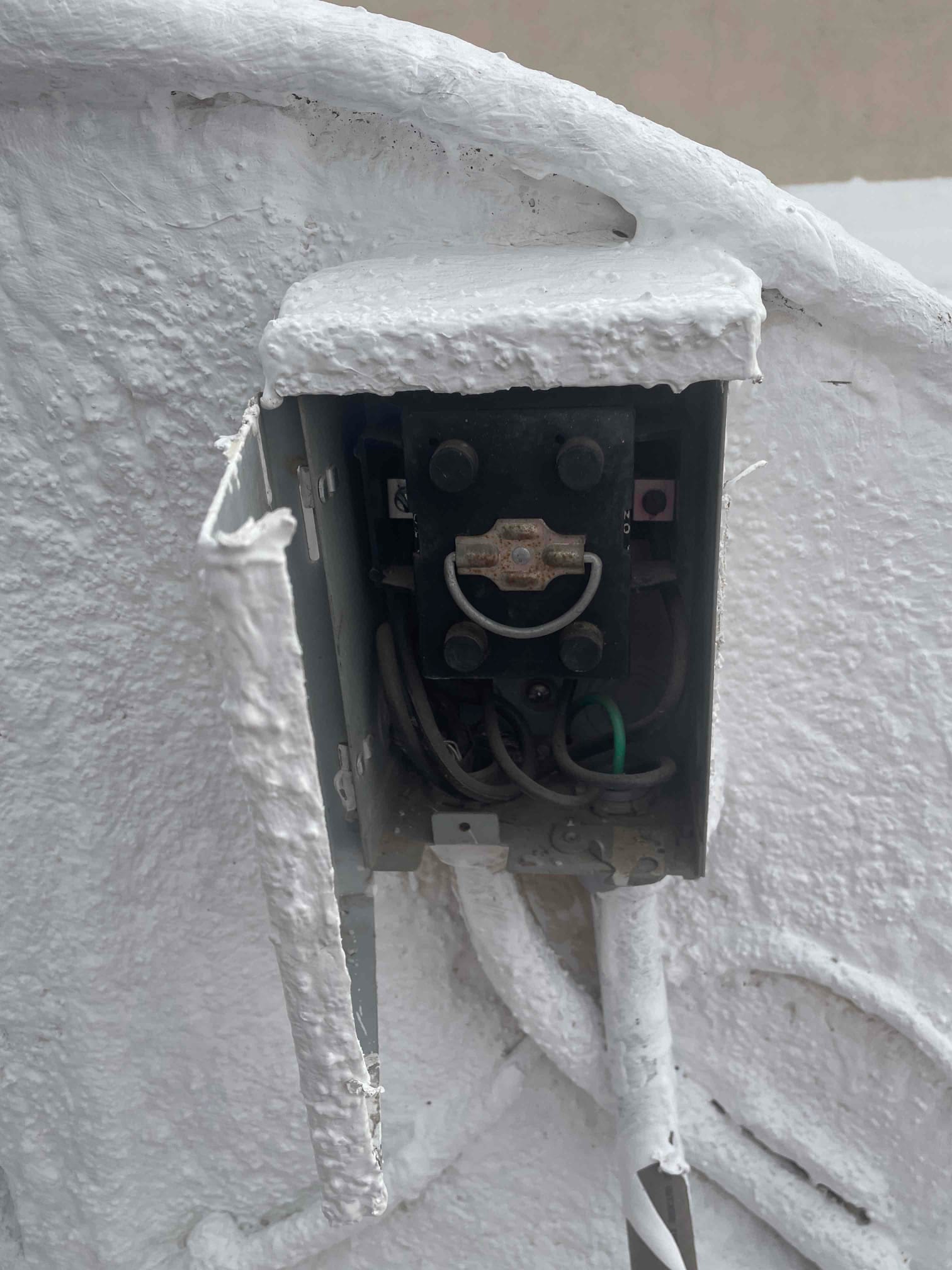 Service disconnect box with pull-out handle and wiring visible, exterior surfaces coated with white paint overspray.