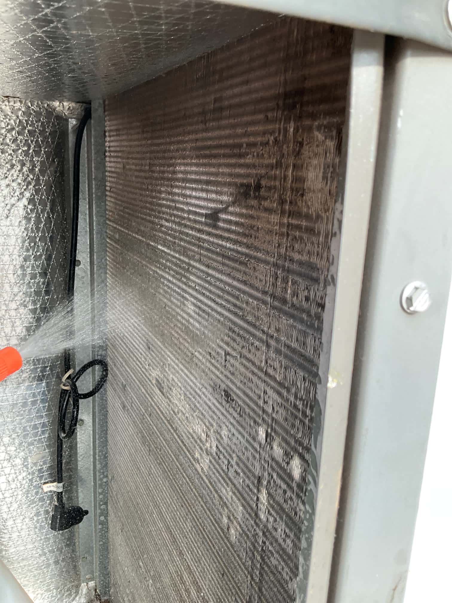 Spray rinses the evaporator coil surface inside the air handler cabinet.