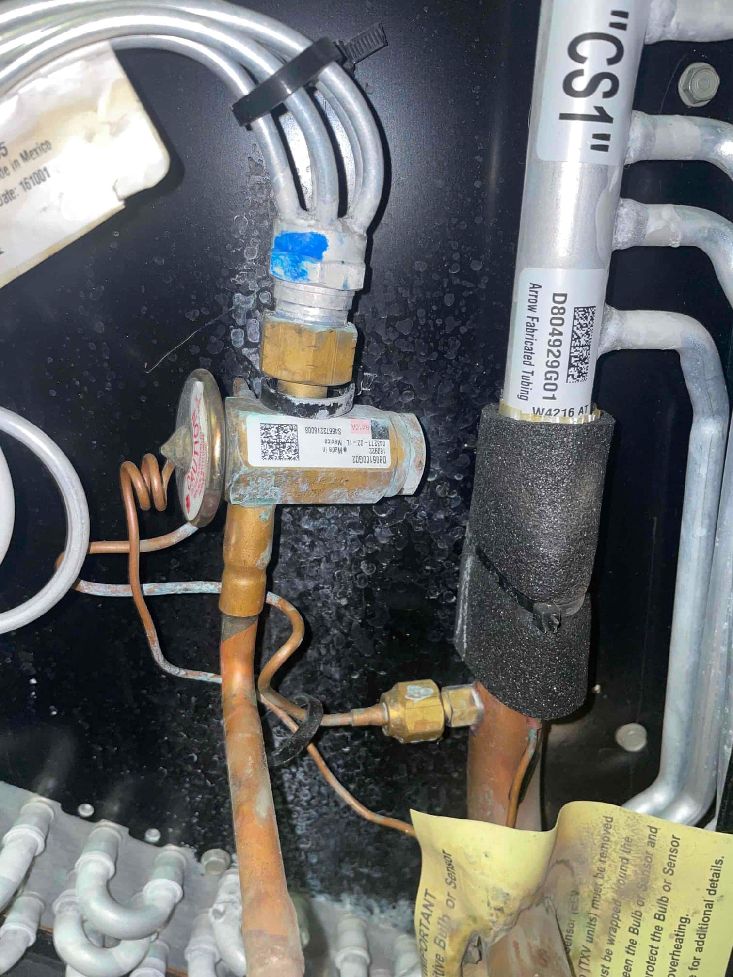 Thermostatic expansion valve with capillary tube and copper refrigerant lines inside the evaporator cabinet, showing surface oxidation on fittings.