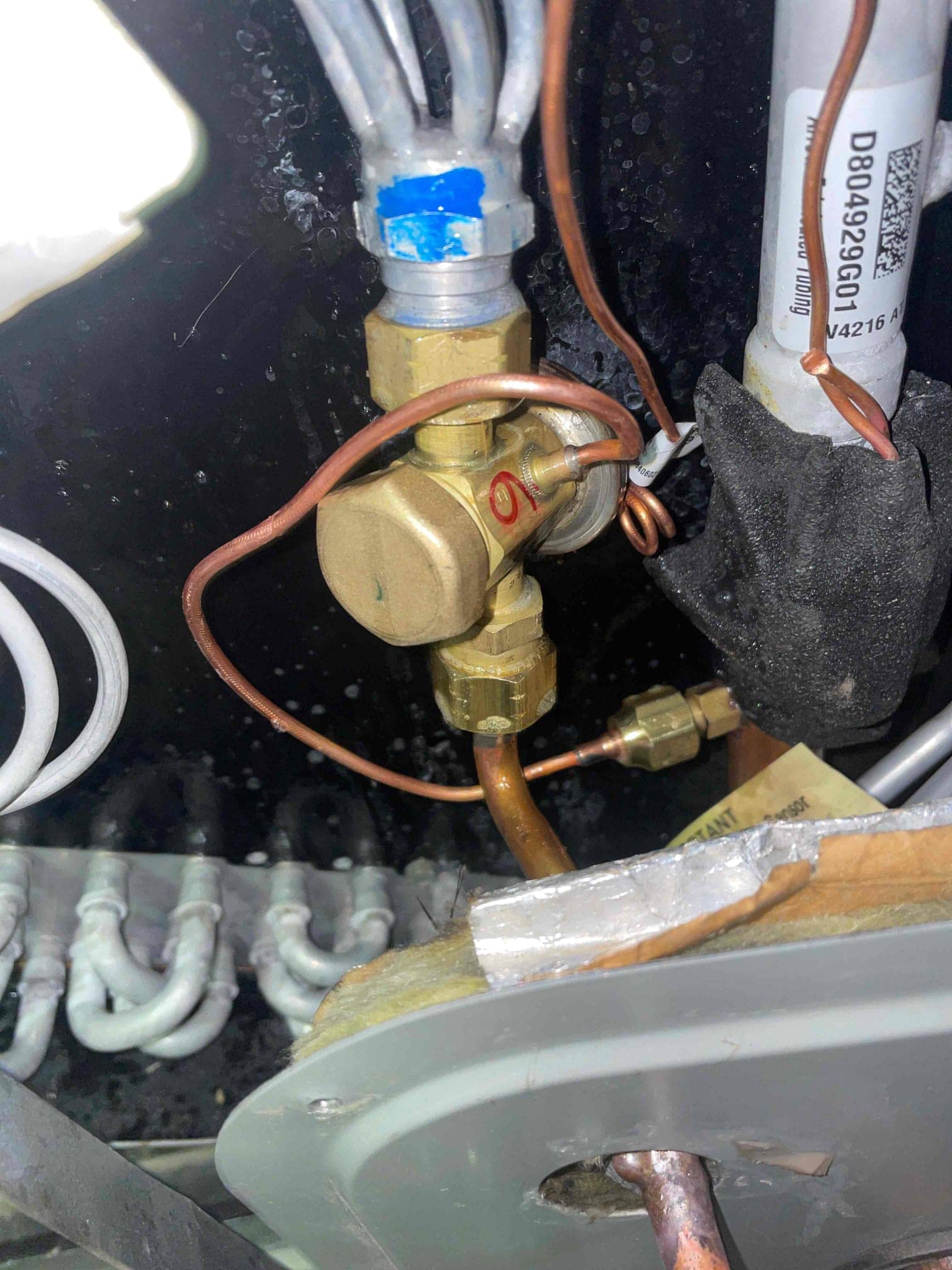 Thermostatic expansion valve with copper lines at the evaporator coil, showing distributor tubes, capillary connections, and surrounding insulation.