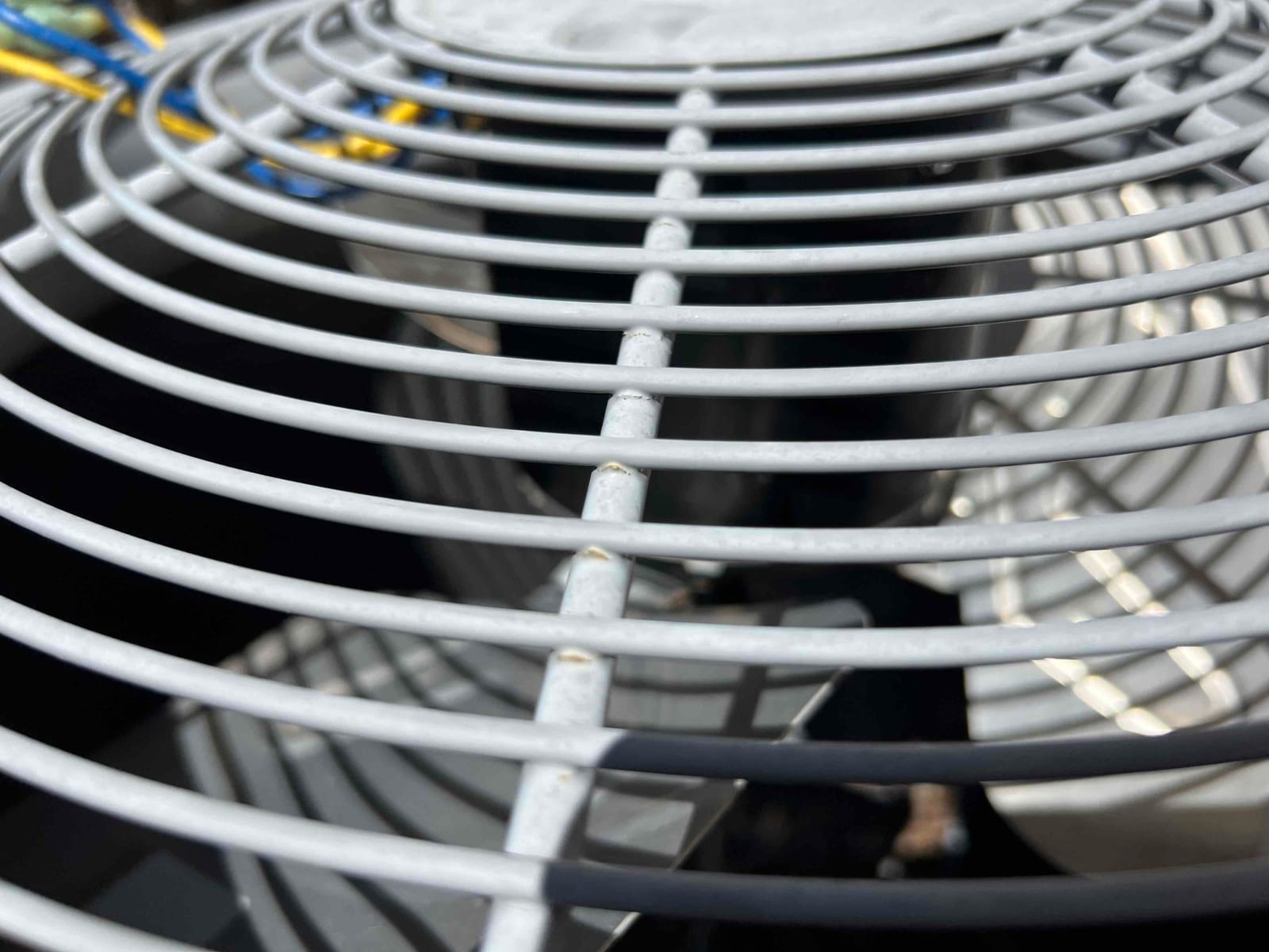 Top grille of an outdoor condenser unit with fan blades and motor visible beneath.
