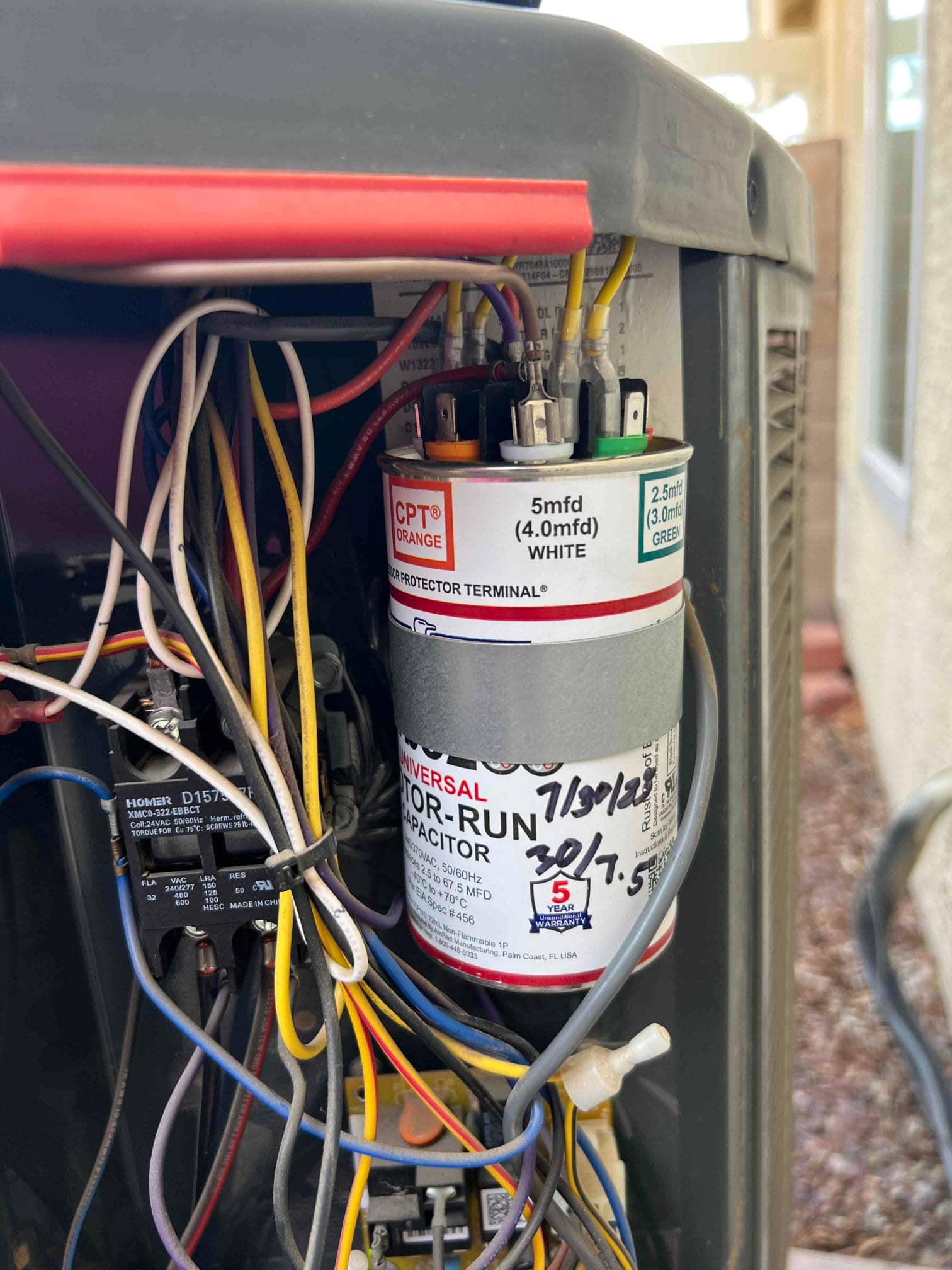Universal motor-run capacitor mounted in an outdoor unit electrical compartment, with wires attached; label shows 5 mfd and 2.5 mfd terminals.