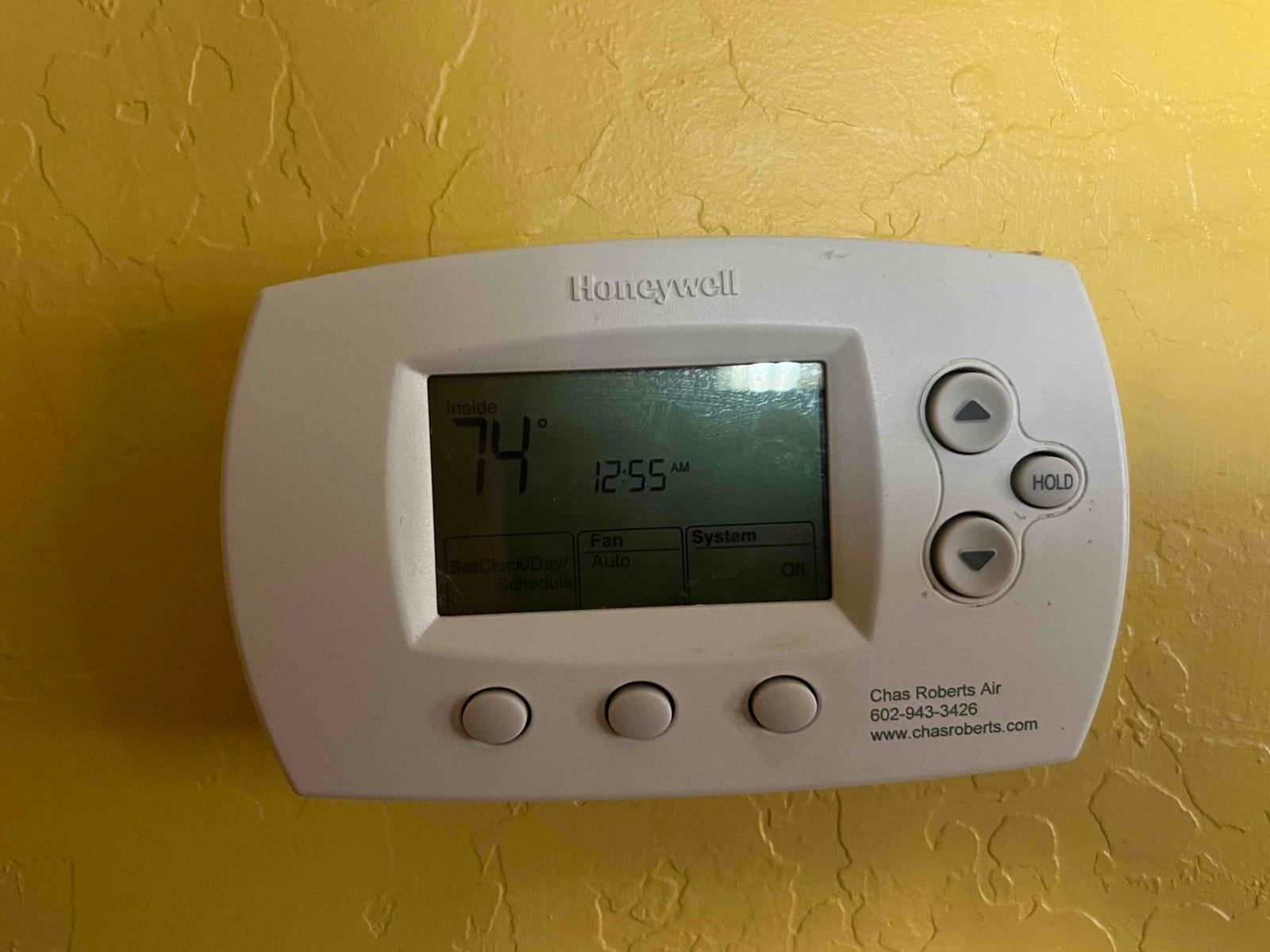 Wall-mounted digital thermostat shows inside temperature 74° and time 12:55 AM, with fan Auto and system Off.