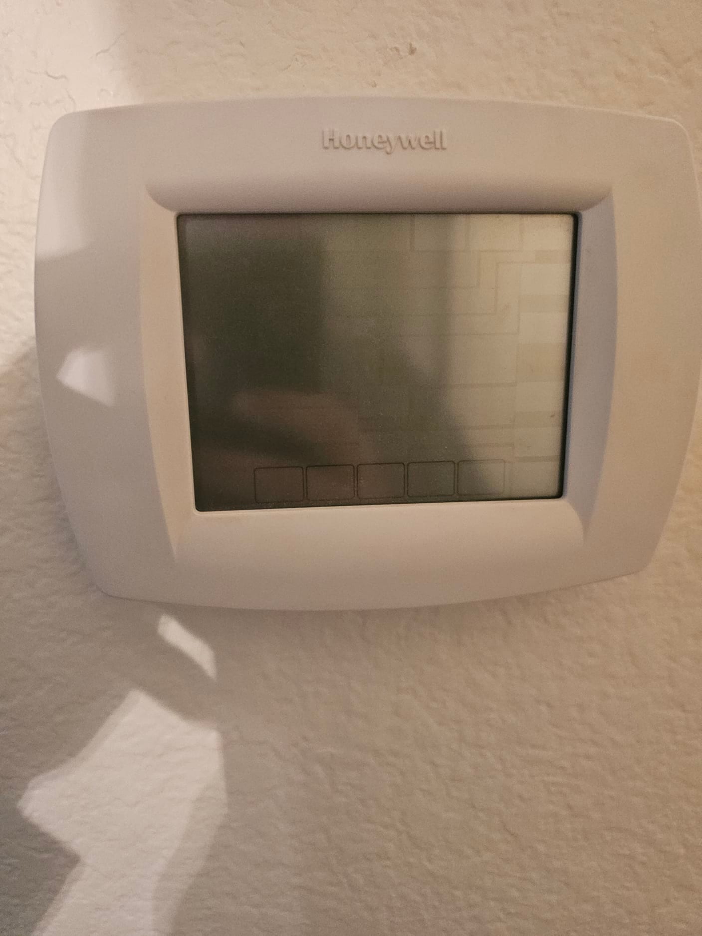 Wall-mounted digital thermostat with an unlit display screen and touch buttons visible at the bottom.