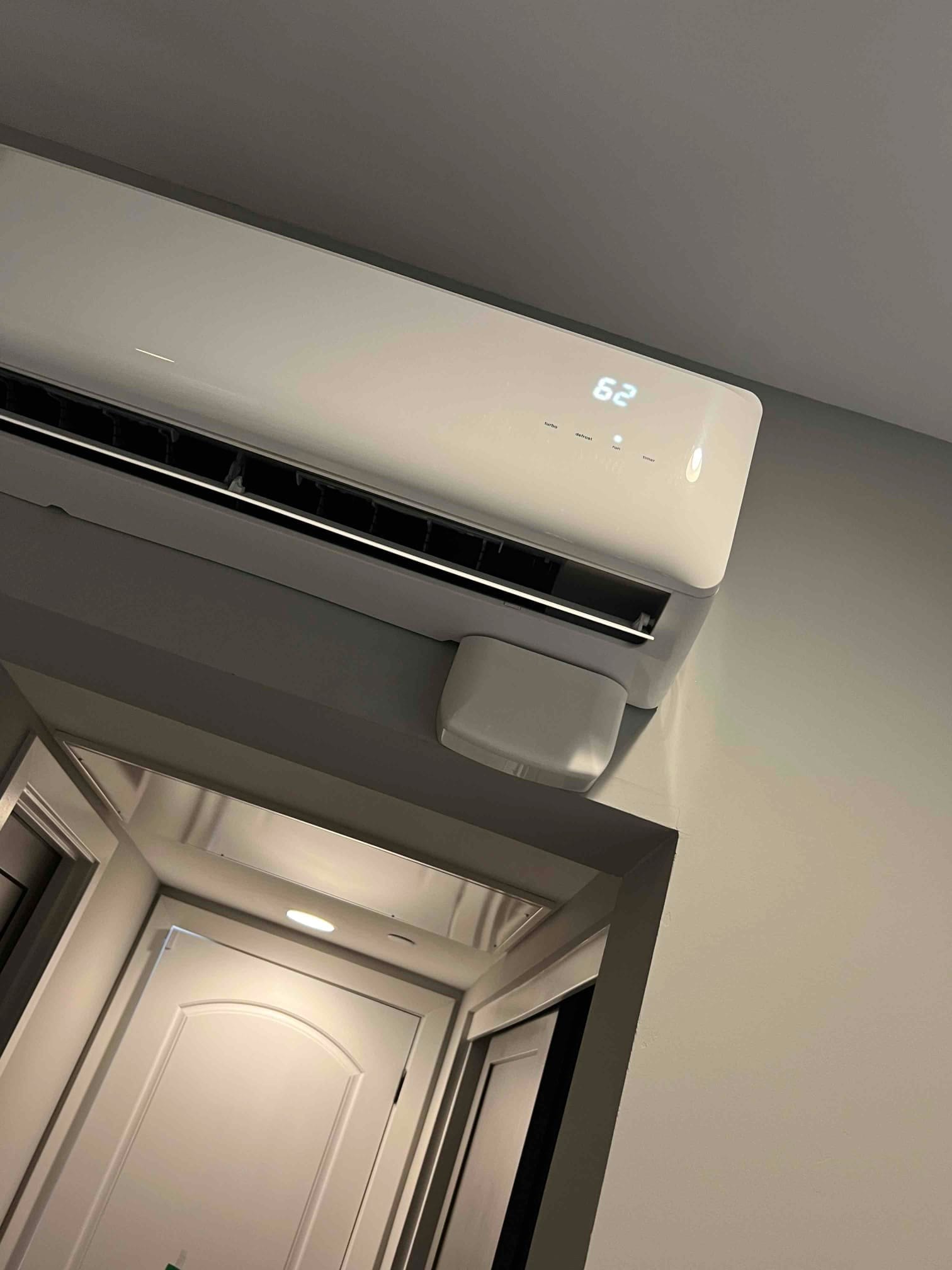 Wall-mounted ductless indoor unit with louvers open; digital display shows 62 on the front panel.