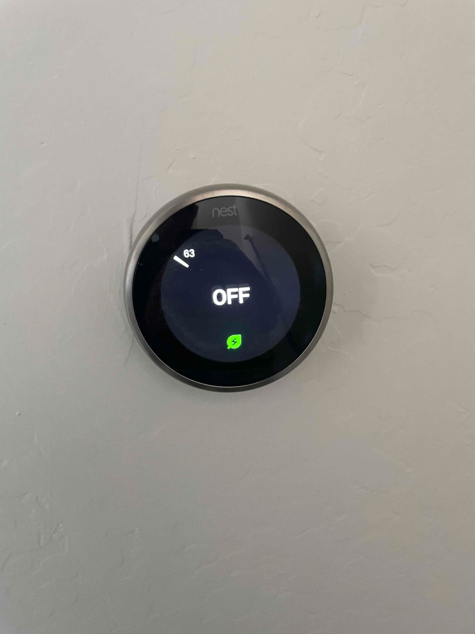Wall-mounted smart thermostat display shows system off with a leaf icon and temperature indicator reading 63.