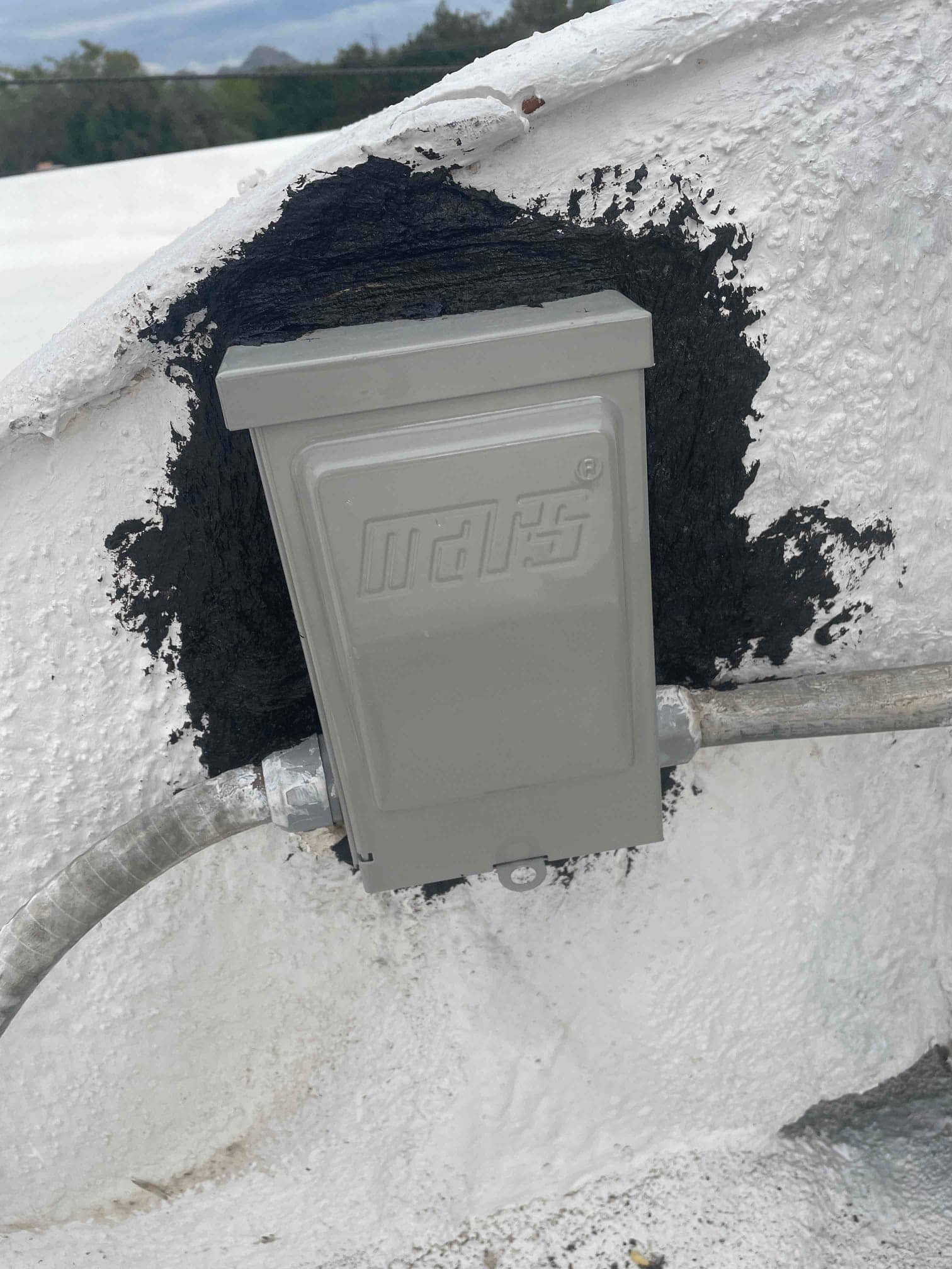 Weatherproof electrical junction box mounted on a rooftop, with flexible metal conduit entering from both sides.
