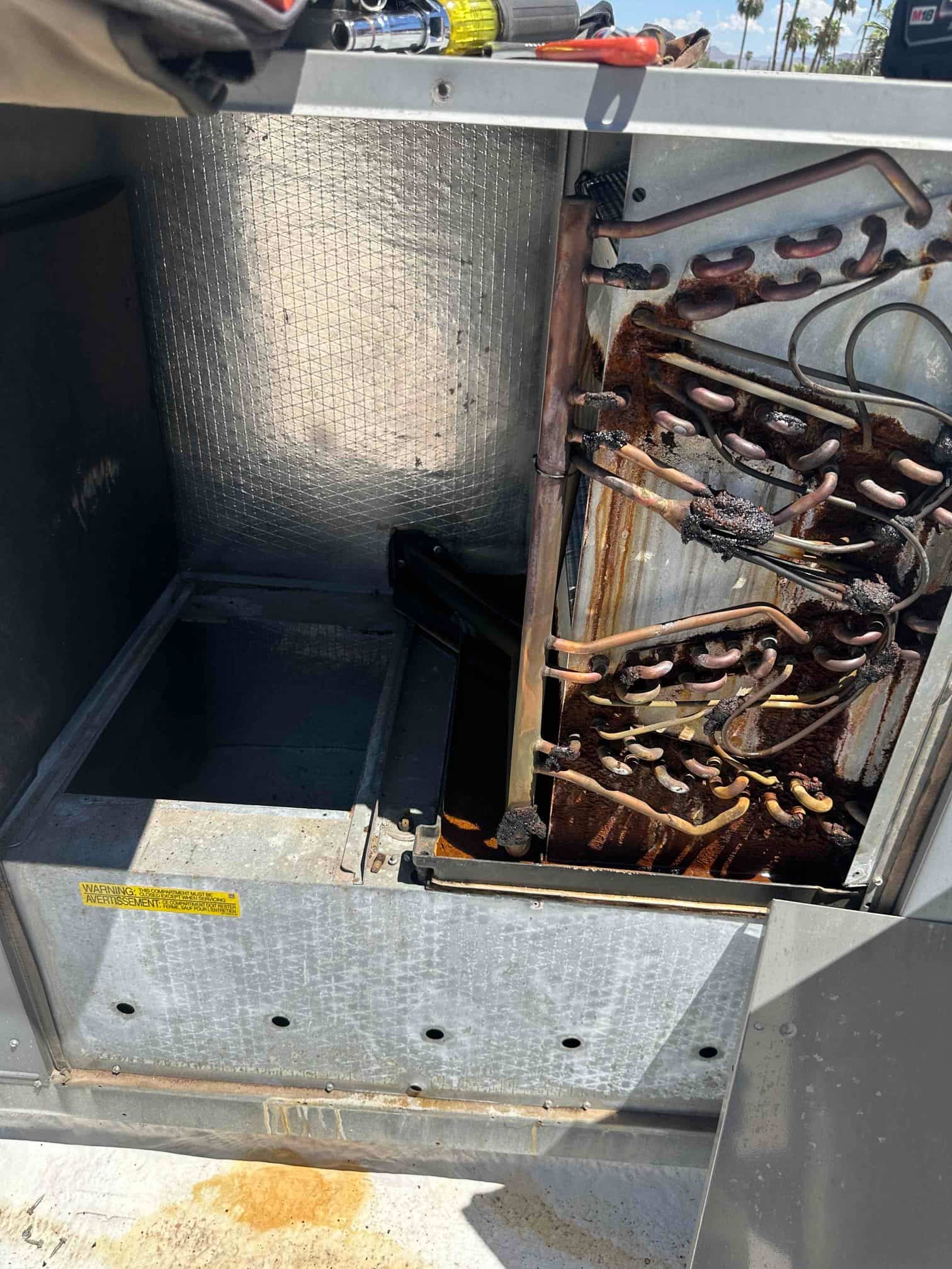 Air handler cabinet open, exposing corroded evaporator coil with rust stains and oxidized copper tubing inside the unit.