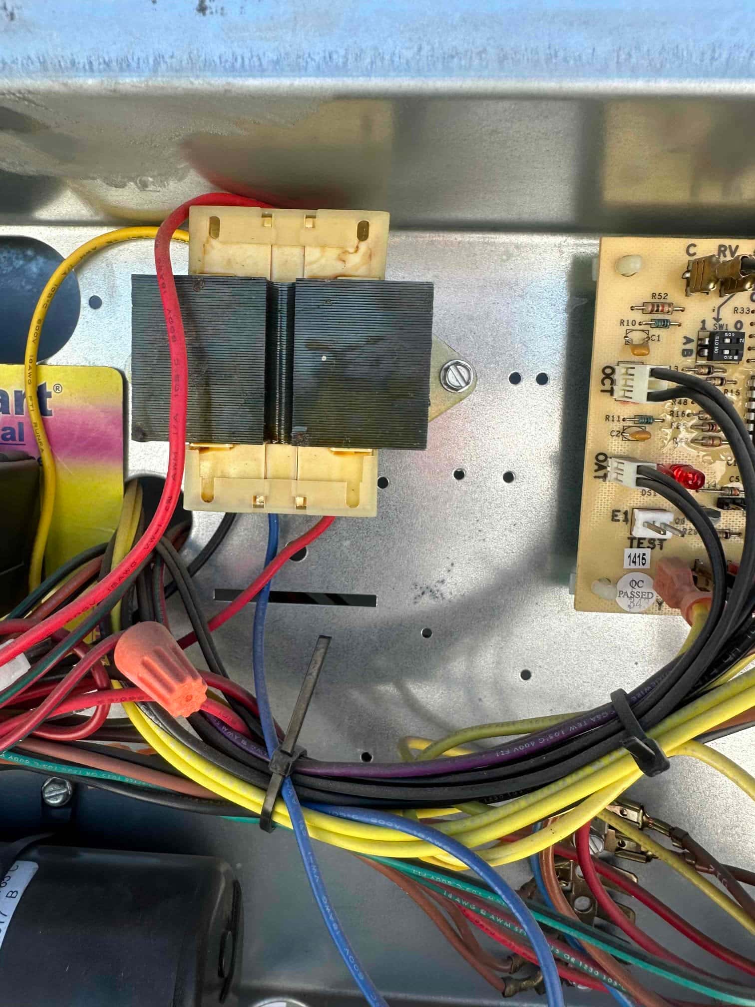 Control compartment showing low-voltage transformer, circuit board with wiring, and bundled conductors routed through the air handler.