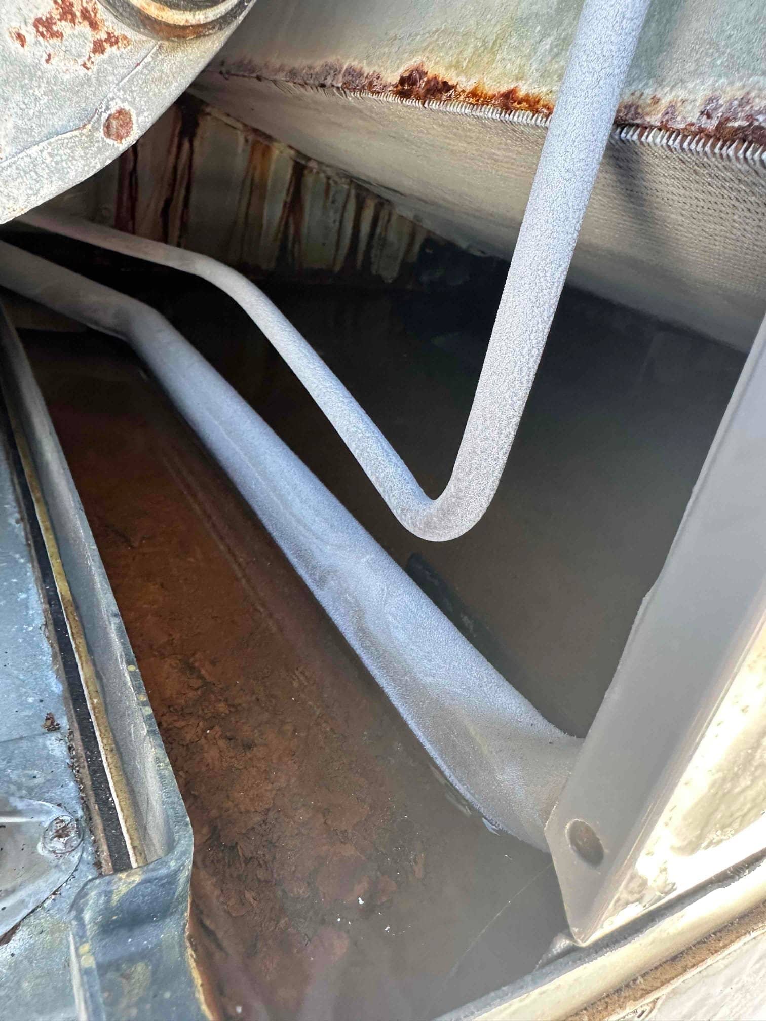 Evaporator coil housing interior showing rusted drain pan and frost accumulation on refrigerant lines and coil surface.