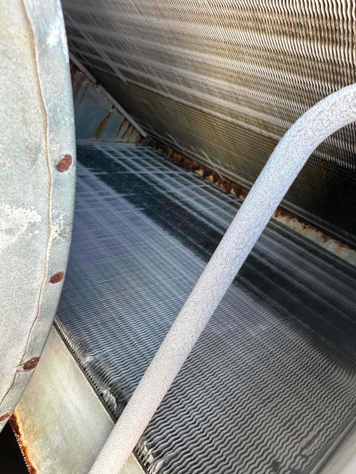 Evaporator coil surface with visible frost accumulation and ice formation along tubing, indicating restricted airflow or low refrigerant conditions.