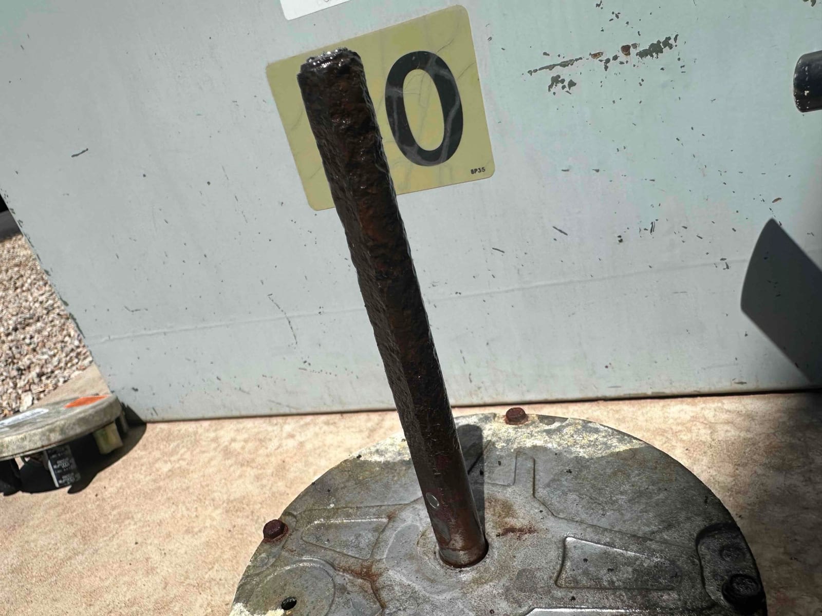 Removed blower motor with heavily rusted shaft and corroded housing resting on the ground for replacement.