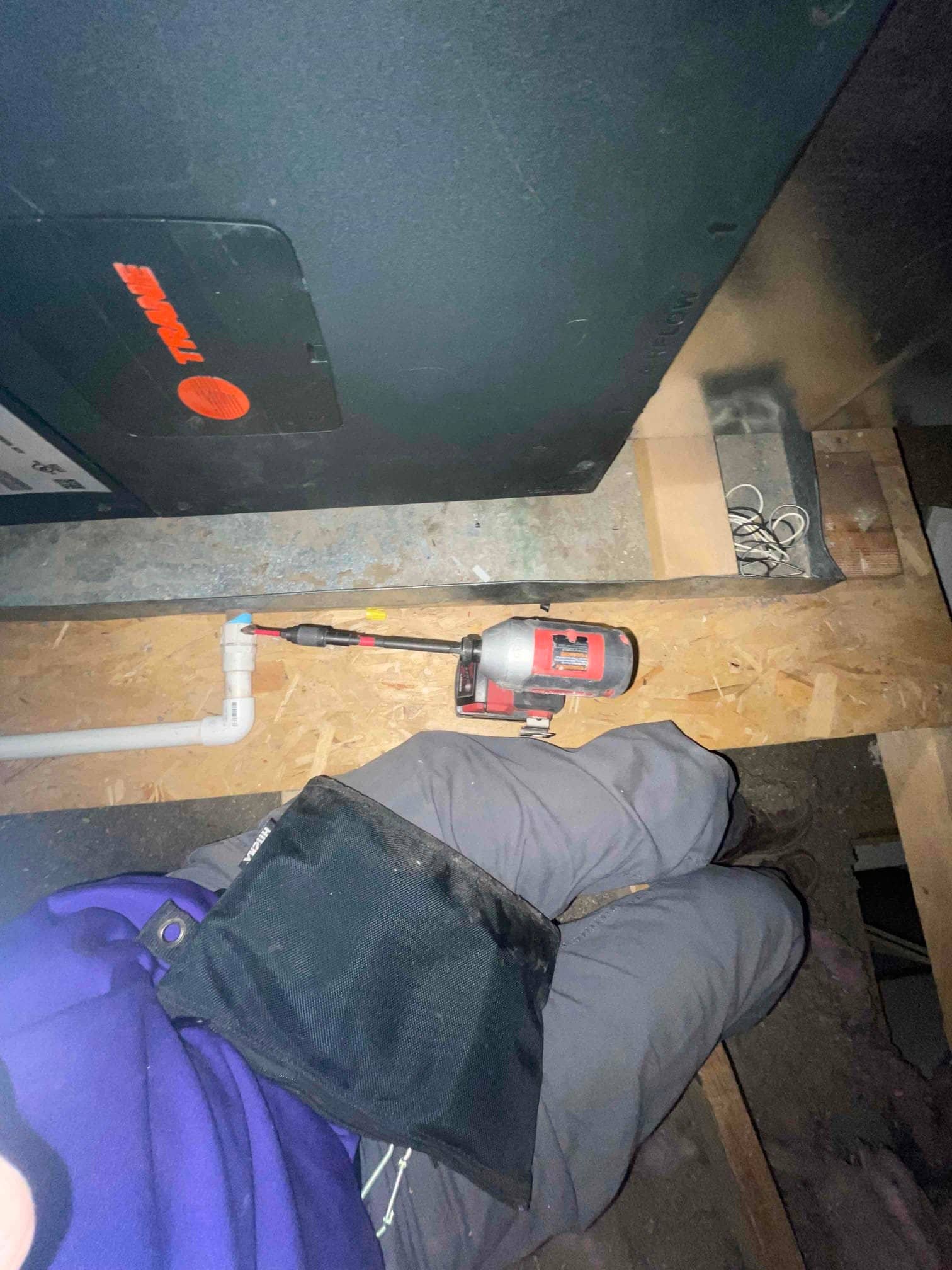 Air handler cabinet in attic with PVC condensate drain and service access panel visible, with technician’s impact driver resting on the joist.