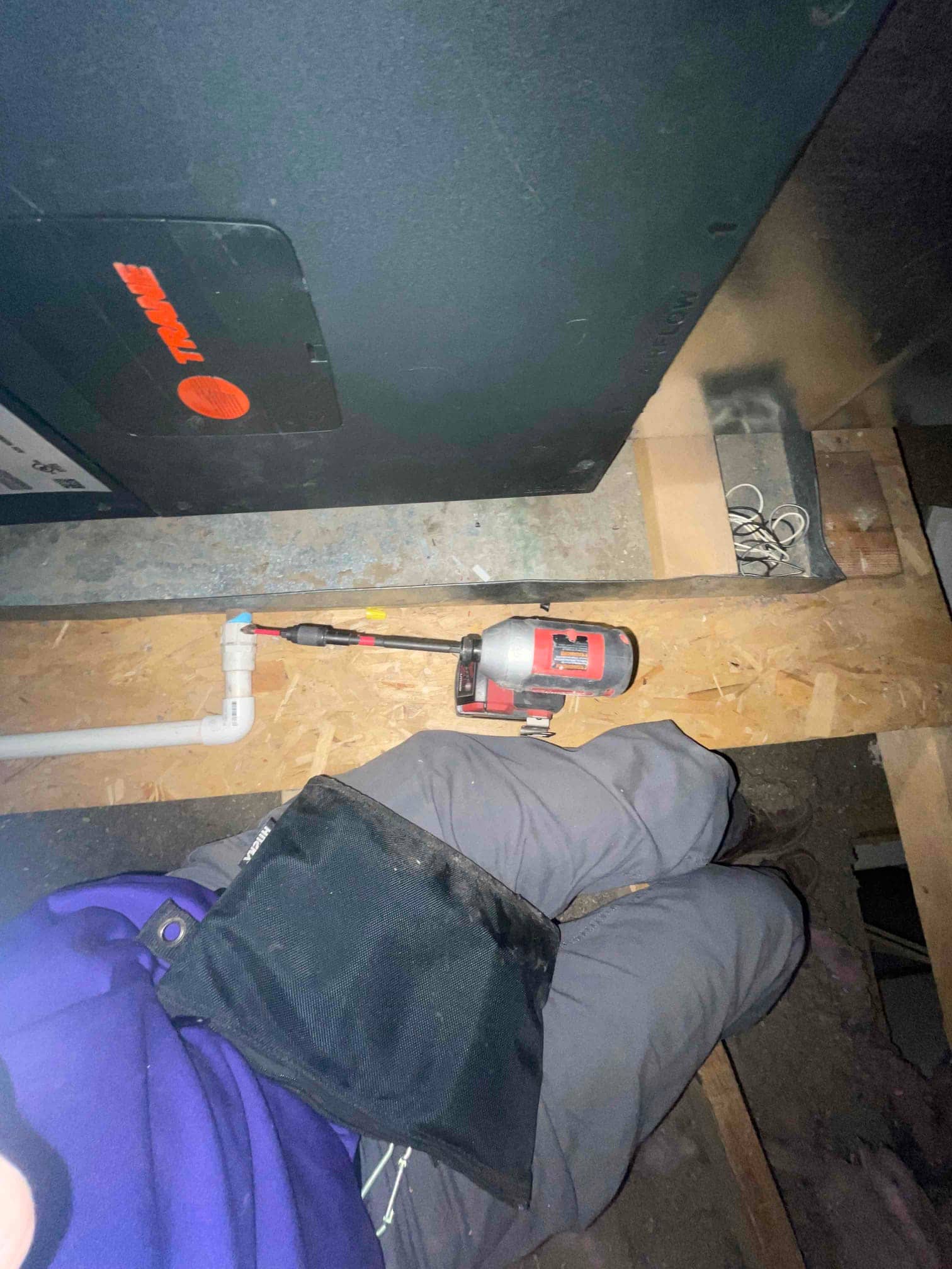Air handler cabinet in attic with PVC condensate drain and service access panel visible near work area.