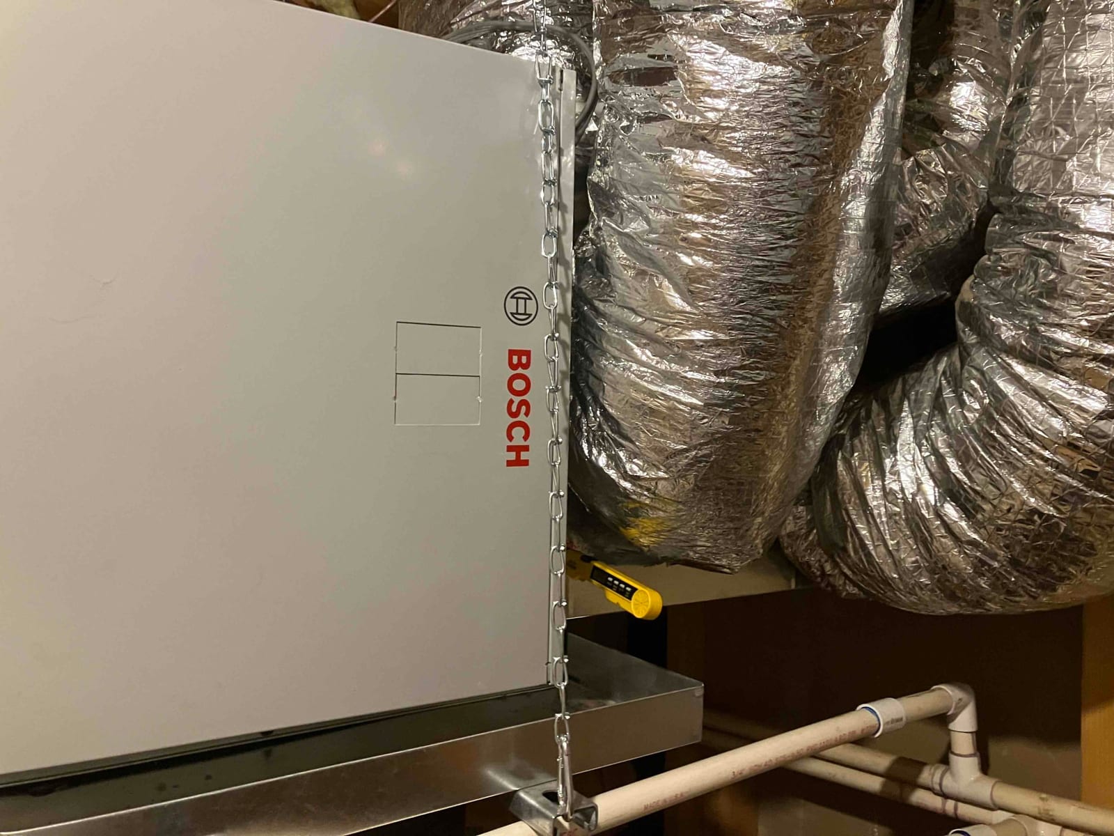 Air handler installed in attic with insulated flex ducts connected, supported by chain, and condensate drain piping routed to trap.