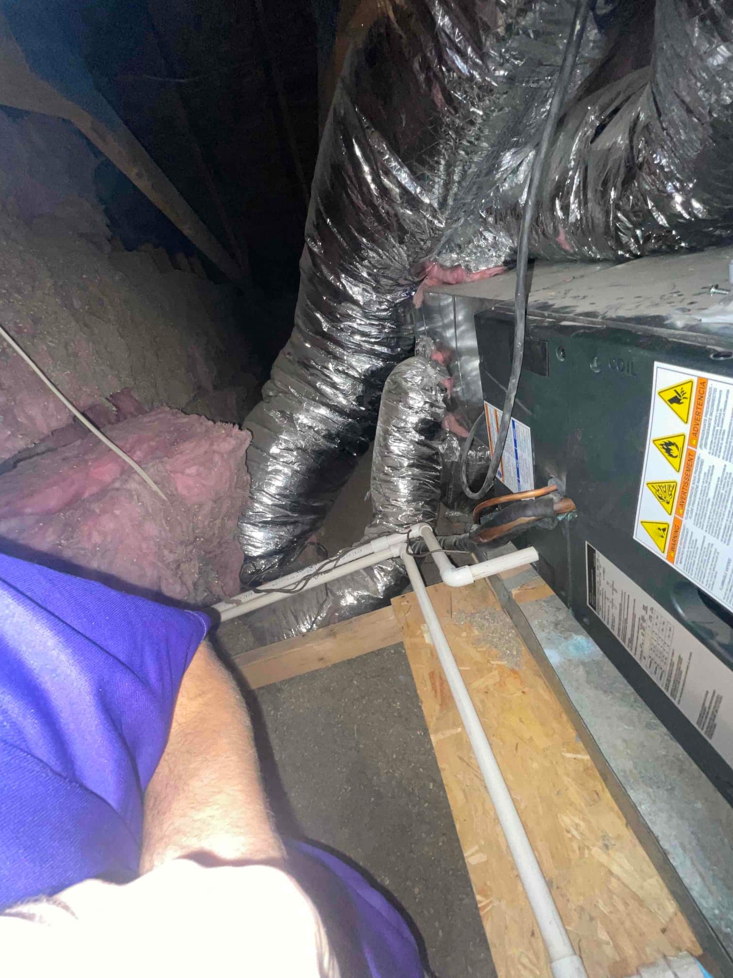 Attic air handler with flex duct connections and PVC condensate drain line on service platform.