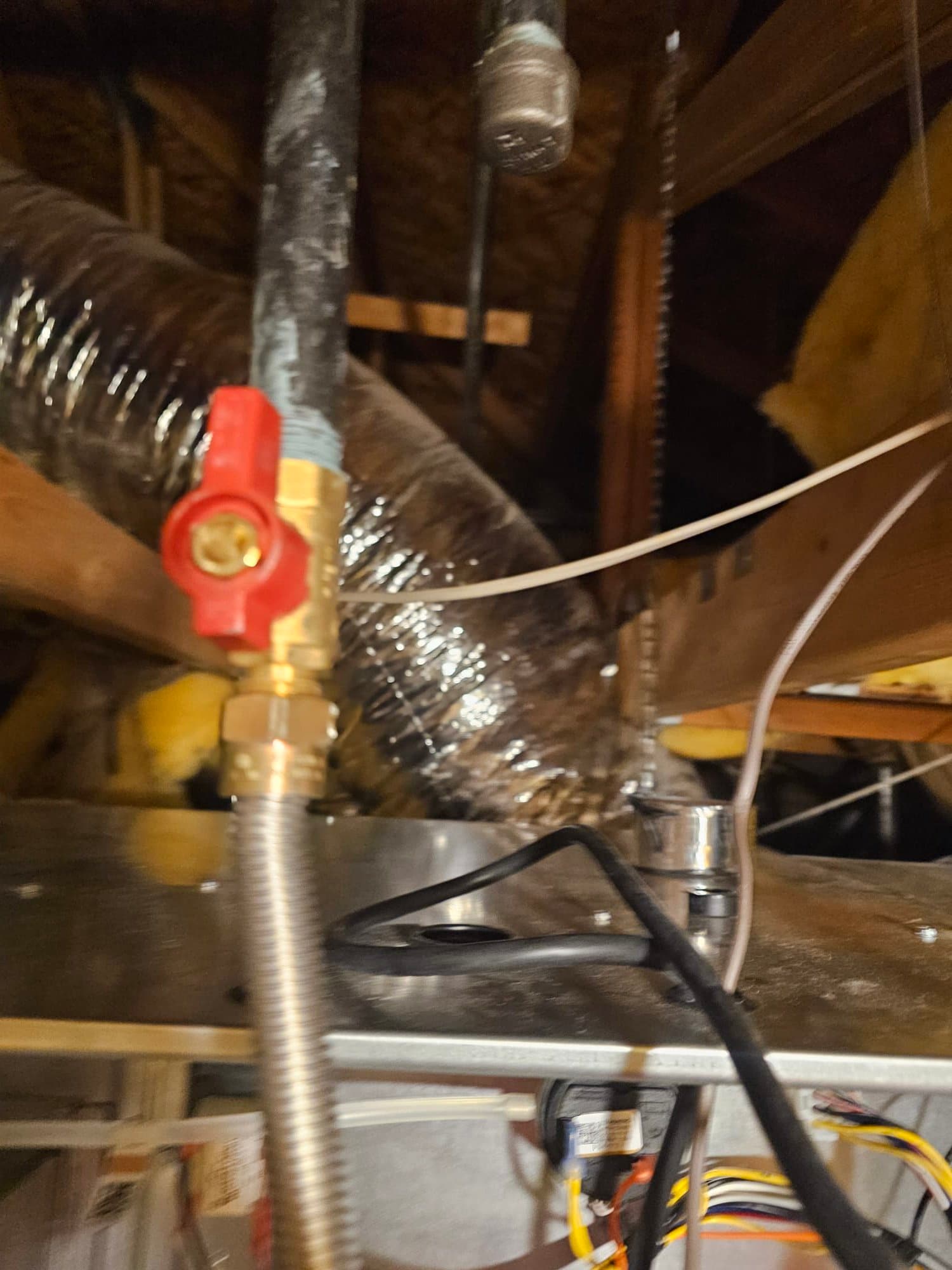 Attic air handler installation showing gas shutoff valve, flexible connector, insulated duct, and wiring routed on the cabinet top.