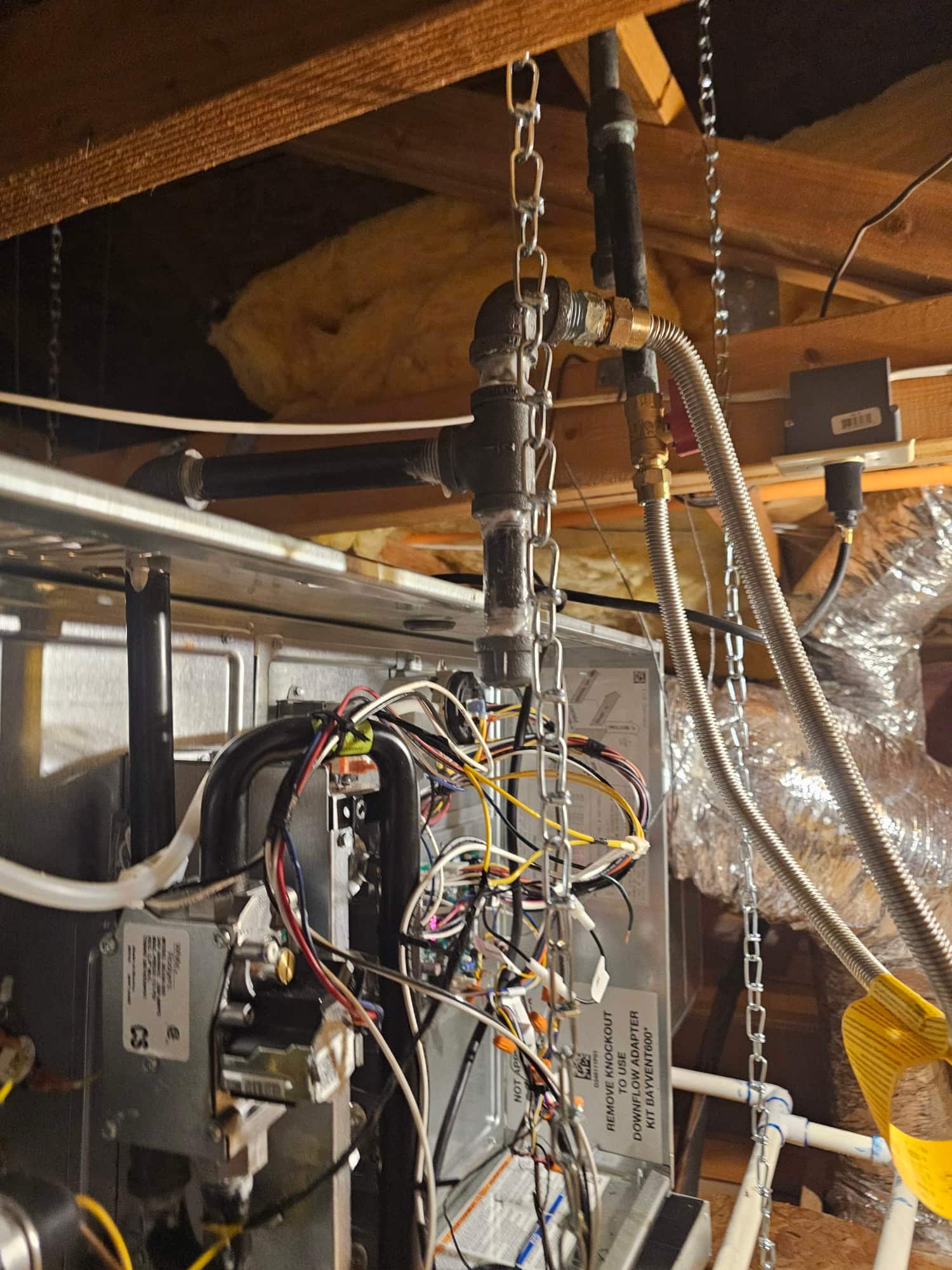 Attic-mounted air handler with hanging support chains, connected gas piping, flexible connector, and organized control wiring during installation.