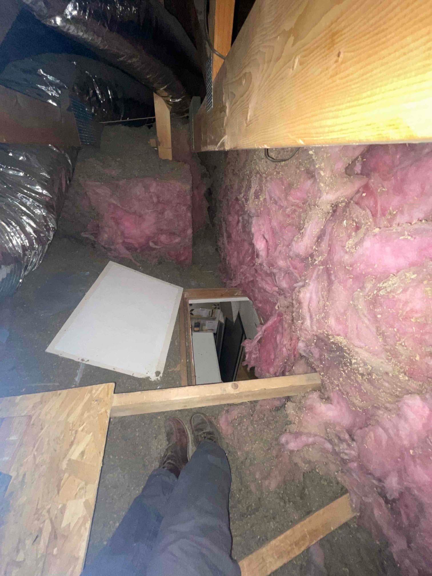 Attic space with flexible insulated ductwork and pink fiberglass insulation near an open access hatch.