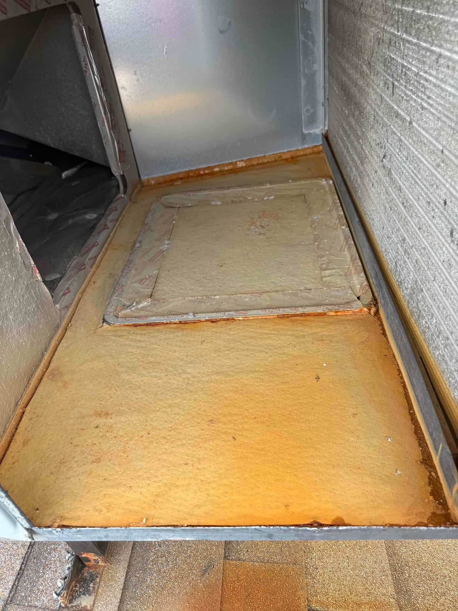 Air handler evaporator section with drain pan showing rust stains and residue, indicating past condensate accumulation and corrosion.