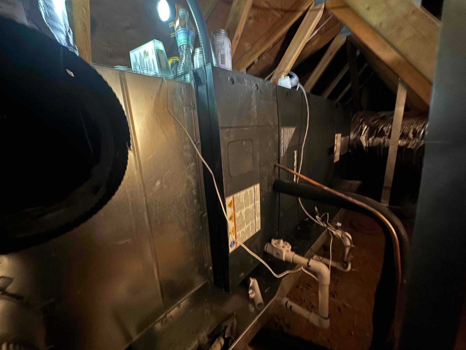 Air handler installed in the attic with insulated refrigerant lines, condensate drain piping, and connected flexible ductwork.