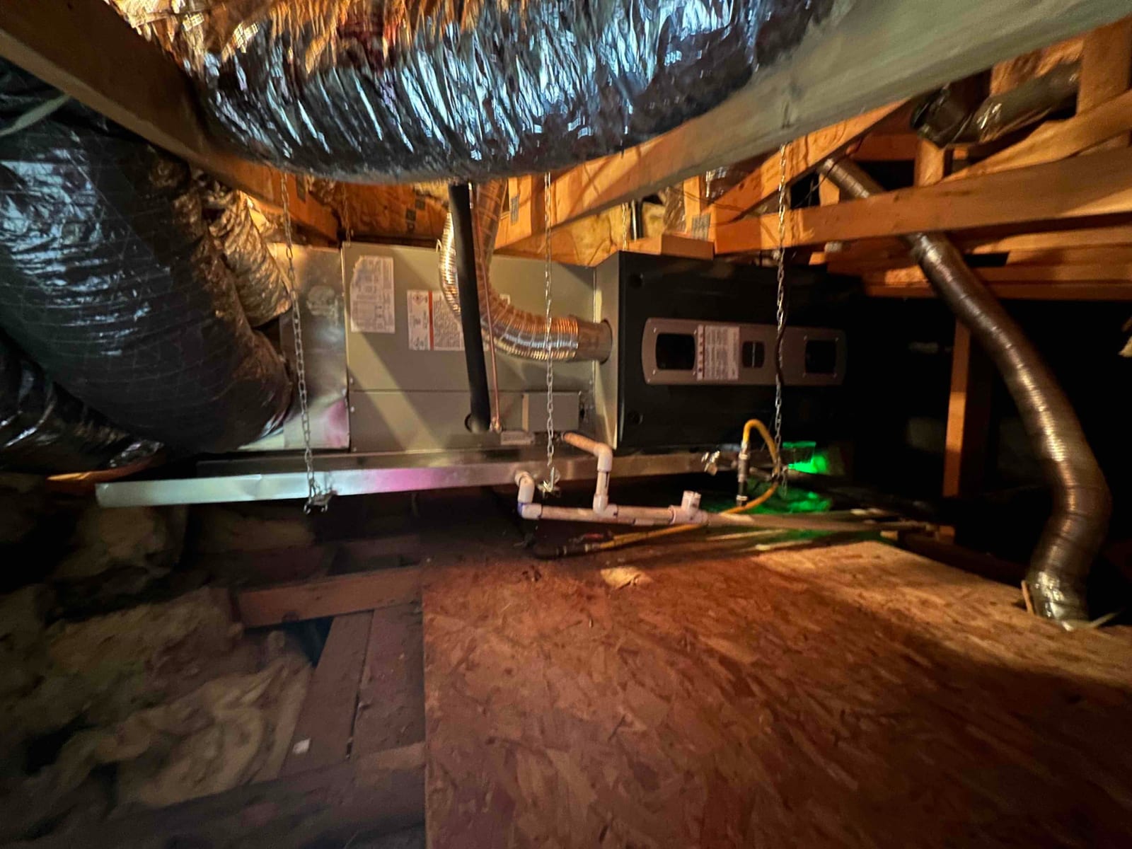 Air handler suspended in attic with insulated duct connections, secondary drain pan, PVC condensate drain, and flexible gas line routed.