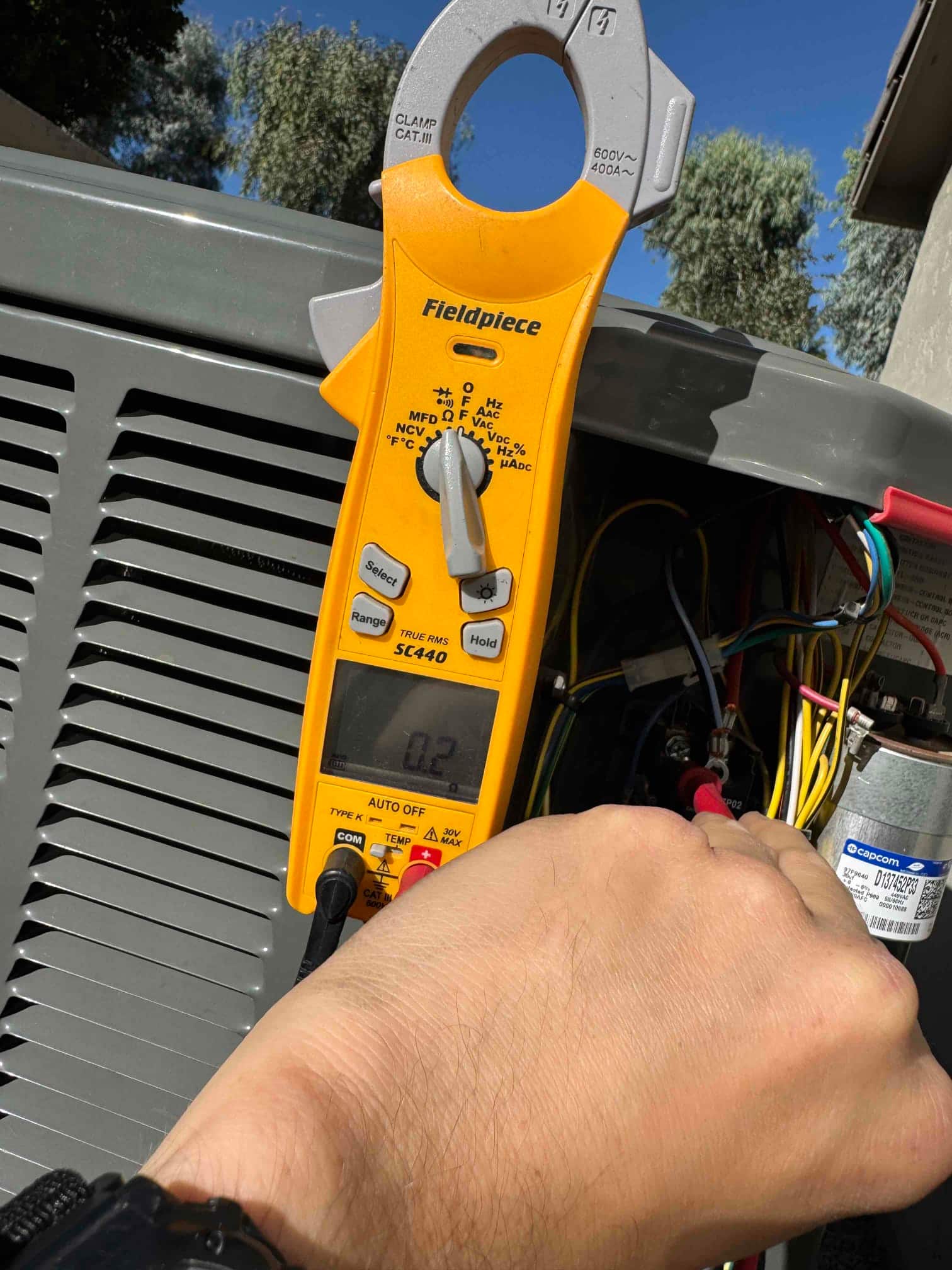 Clamp meter displays 0.2 A while measuring current on a conductor at the outdoor condenser unit.