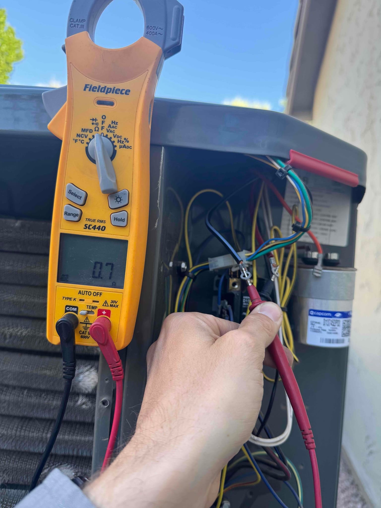 Clamp meter displays 0.7 A while measuring current on a conductor inside the outdoor condenser cabinet.