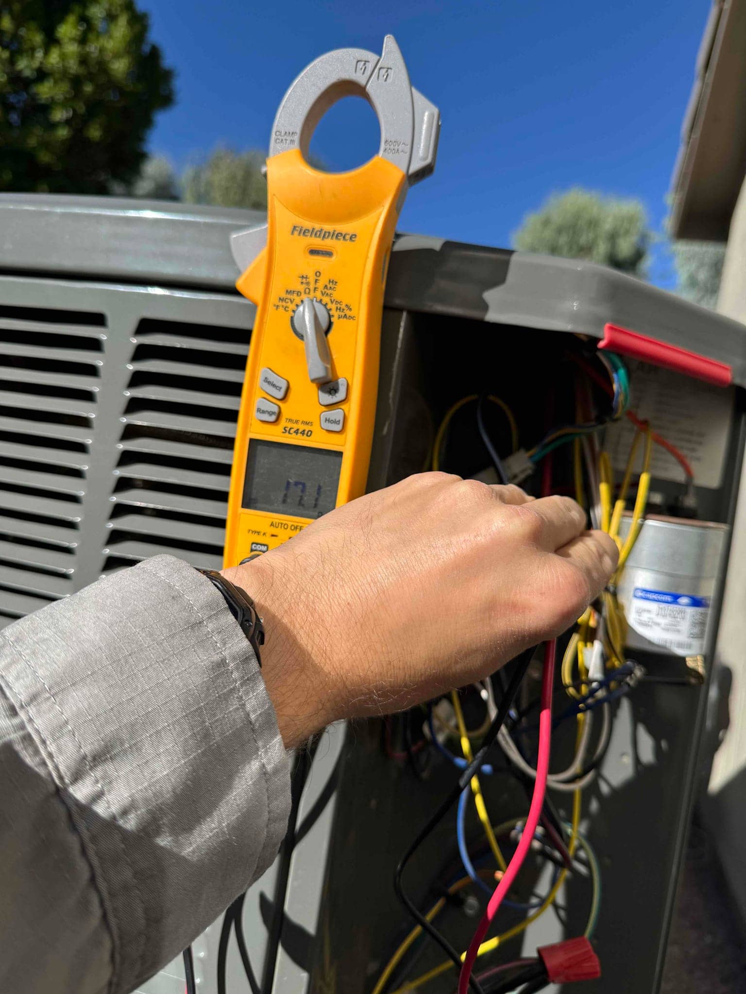 Clamp meter measures 0 A on a conductor inside the outdoor condenser control compartment during air conditioning repair.