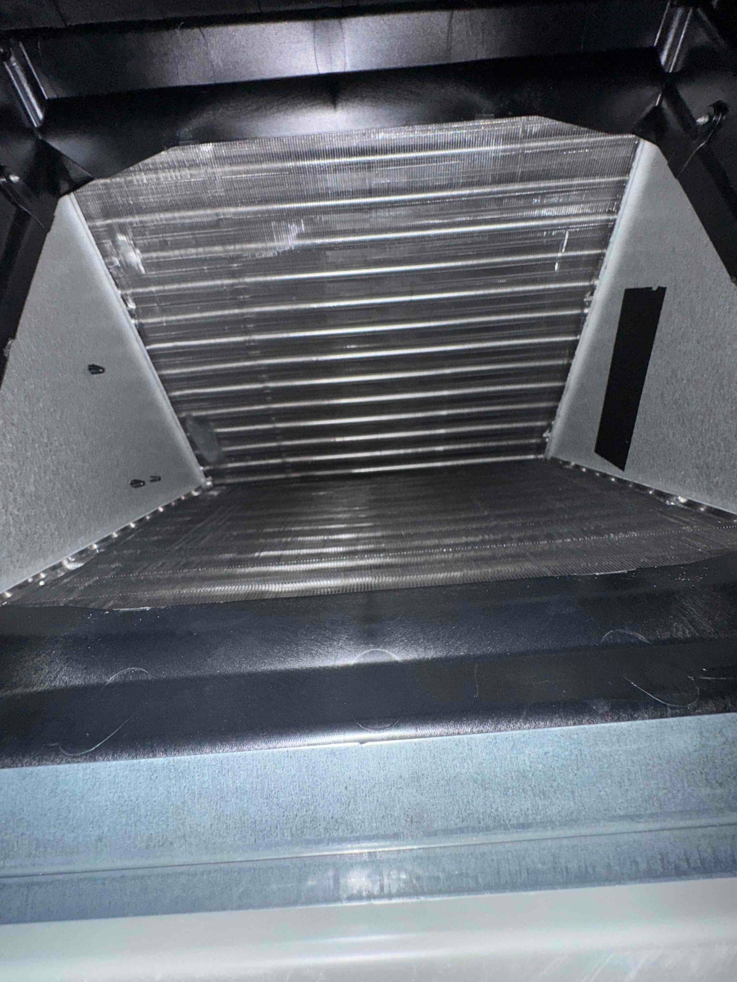 Clean indoor evaporator coil and housing visible inside the air handler, showing straight fins and intact drain pan area.