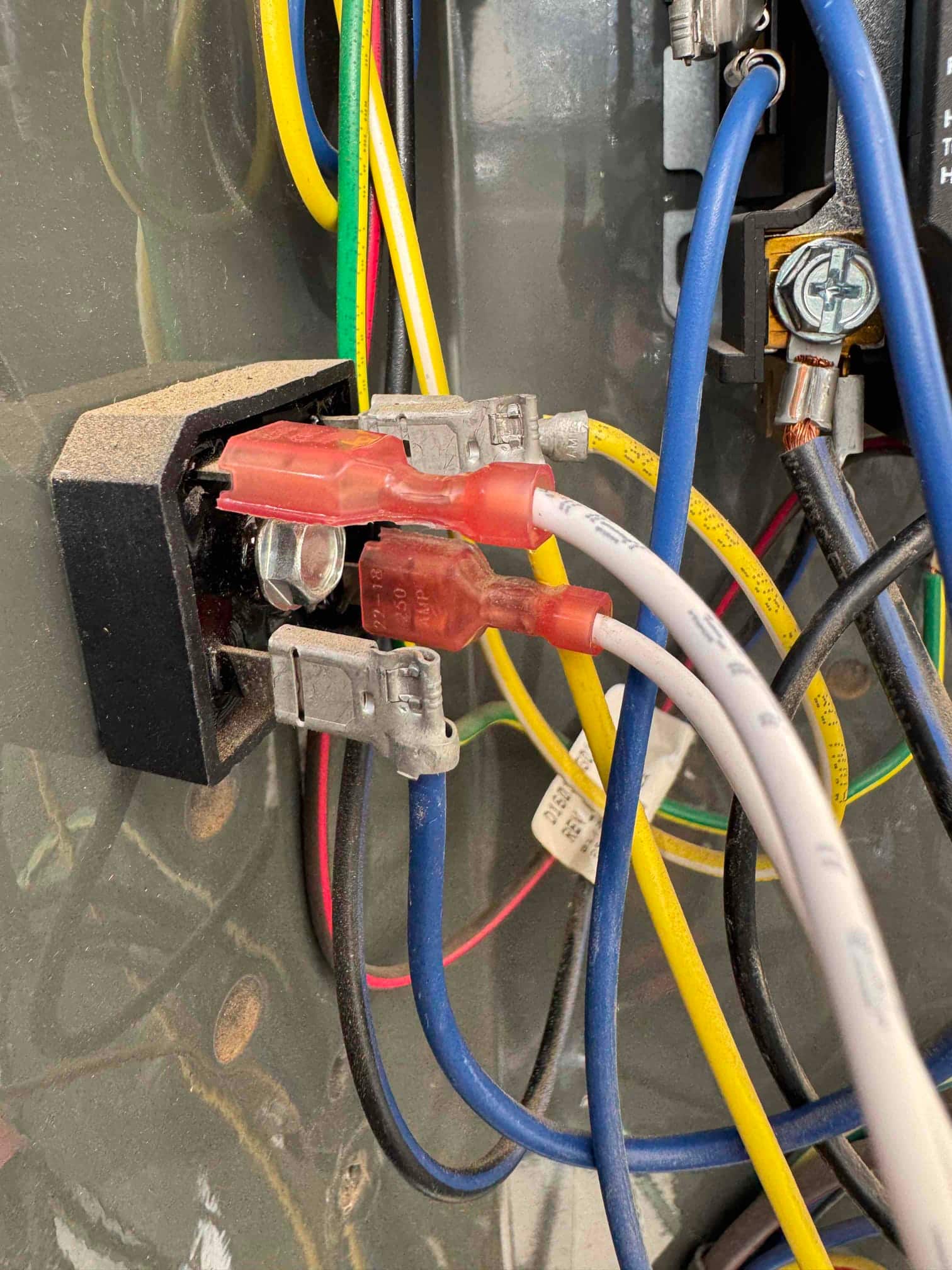 Close-up of a control relay with red insulated spade terminals and connected blue and white wires inside the condenser cabinet.