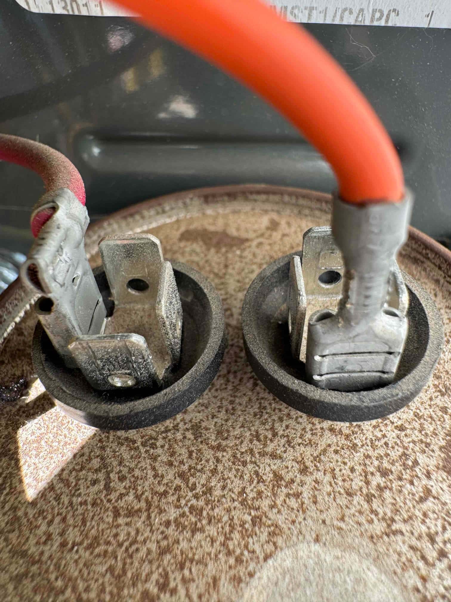 Close-up of two electrical spade terminals with red insulated wires connected to an HVAC component.