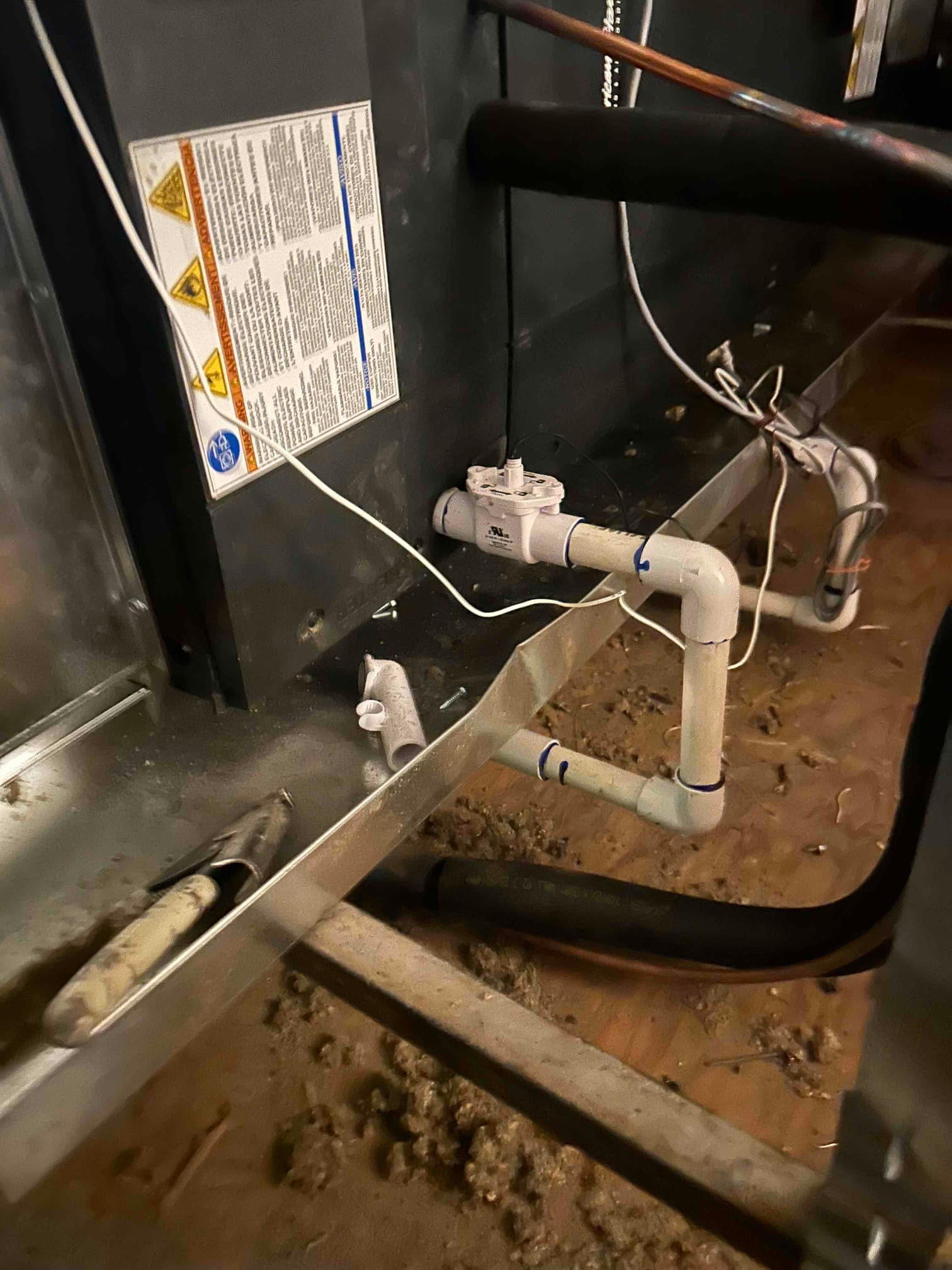Condensate drain assembly with float safety switch installed beneath a new indoor air handler, with insulated refrigerant line nearby.