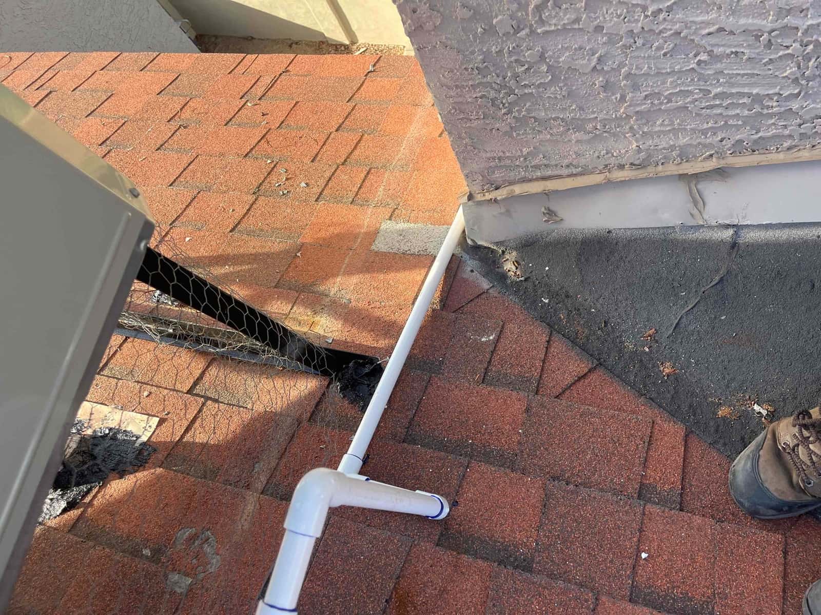 Condensate drain line routed across shingle roof to wall flashing, with fittings secured and penetration sealed.