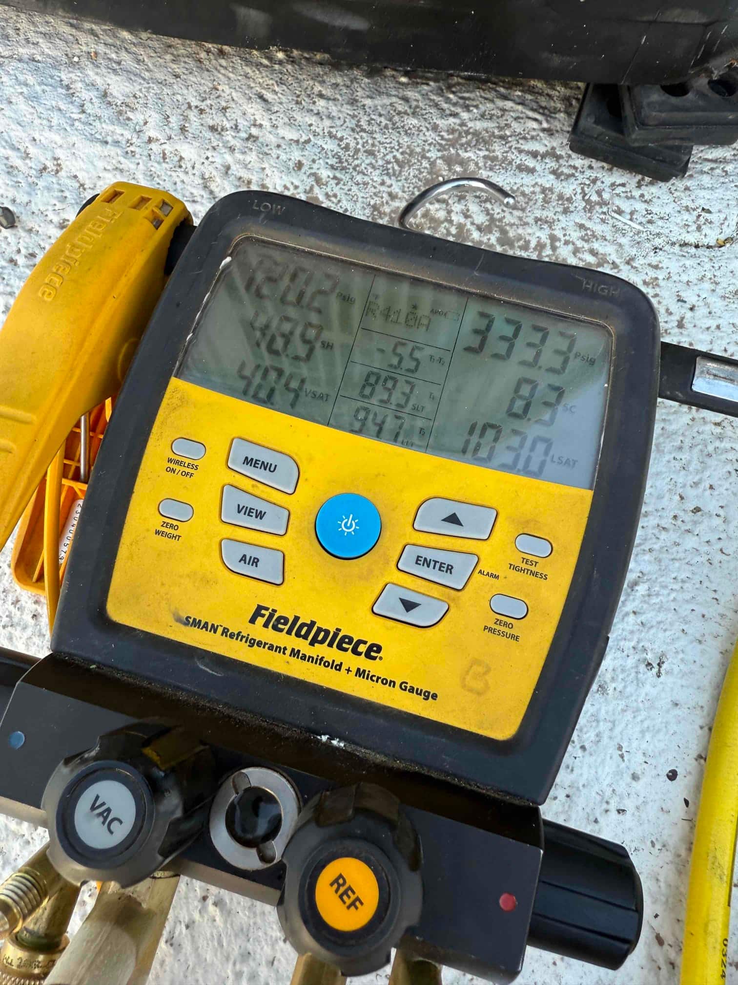 Digital manifold gauge on the outdoor unit shows operating suction and liquid pressures during system commissioning.