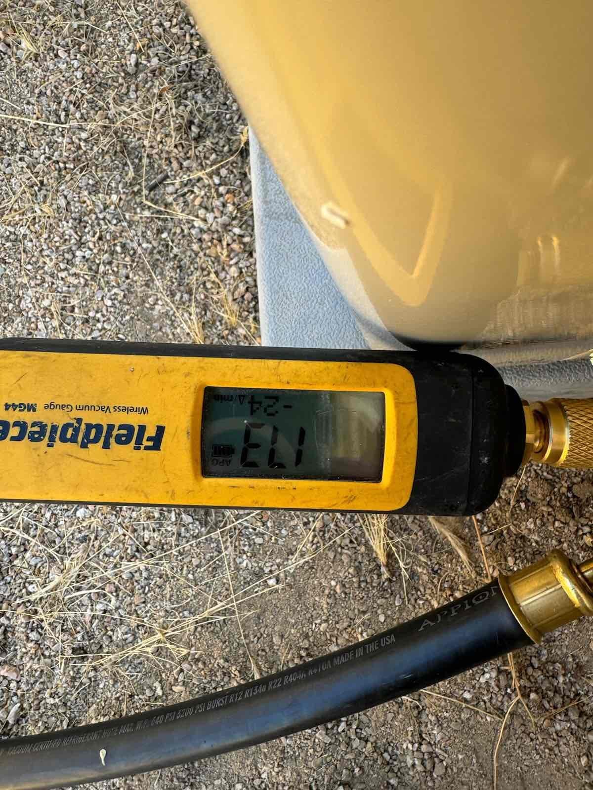 Digital micron gauge connected to the system during evacuation, screen reading 113 microns near the outdoor unit.