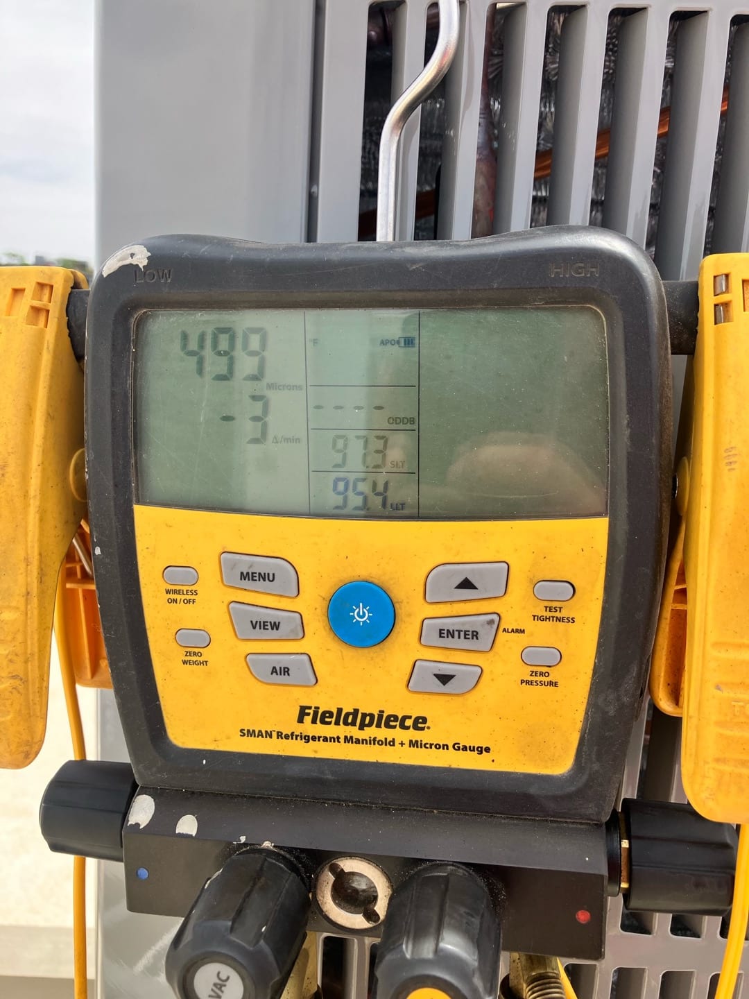 Digital micron gauge on the outdoor unit displays 499 microns, confirming a deep vacuum during system evacuation.