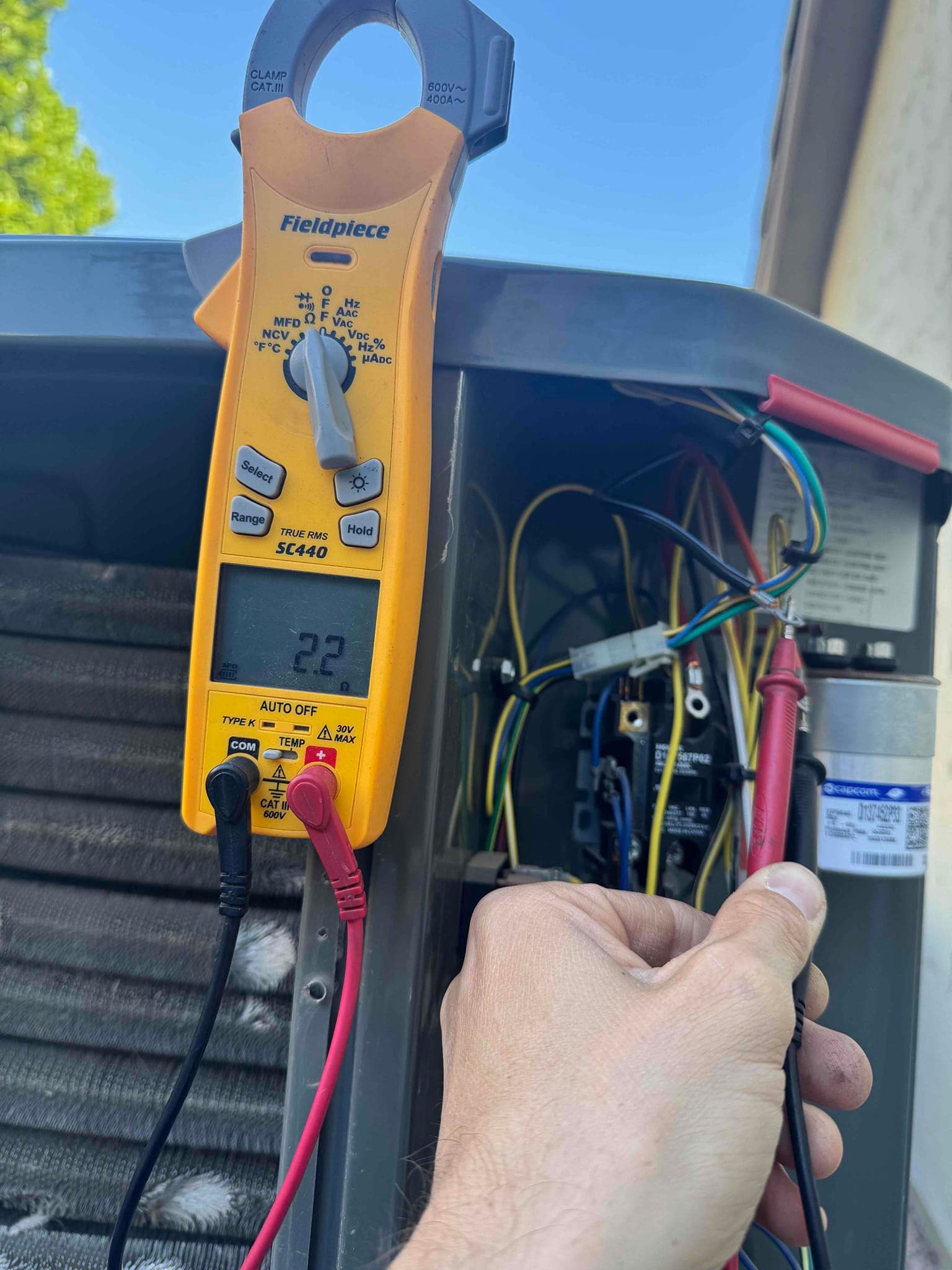 Digital multimeter displays 22 V while red and black probes contact terminals inside the outdoor condenser control compartment.