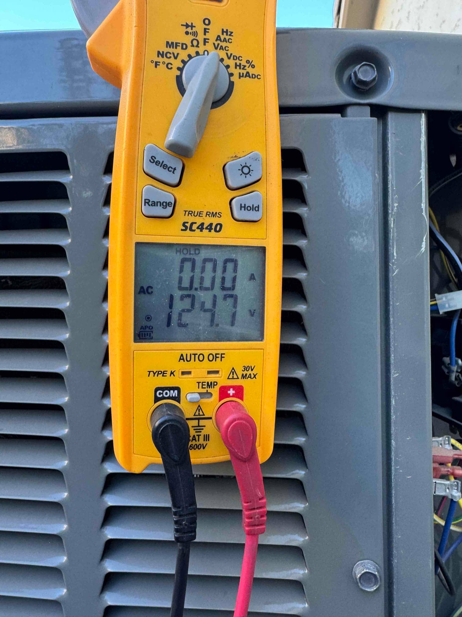Digital multimeter shows 124.7 V AC with probes connected to the unit’s electrical terminals.