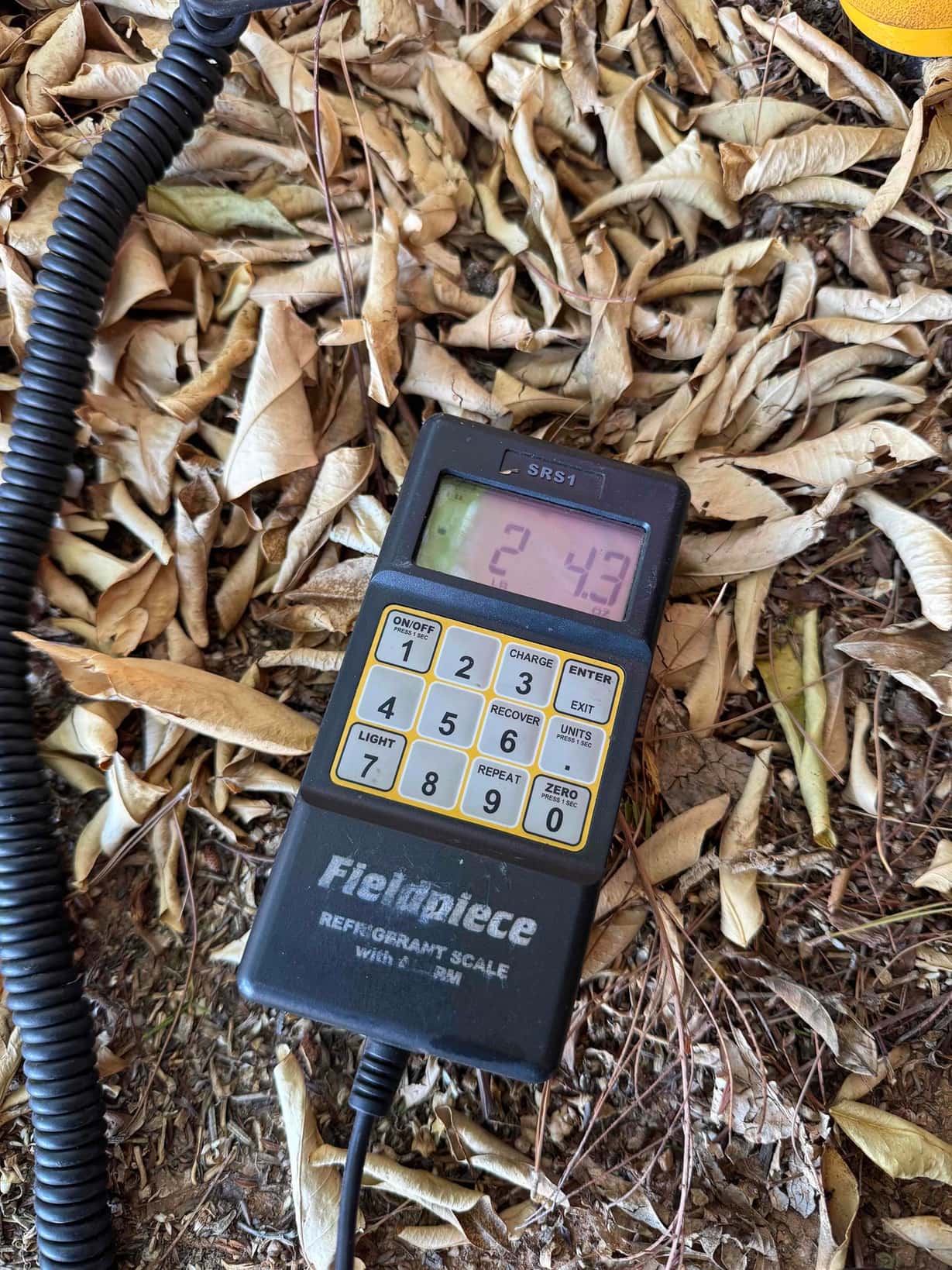 Digital refrigerant scale on the ground displays 2.43 lb during an R-410A recharge.