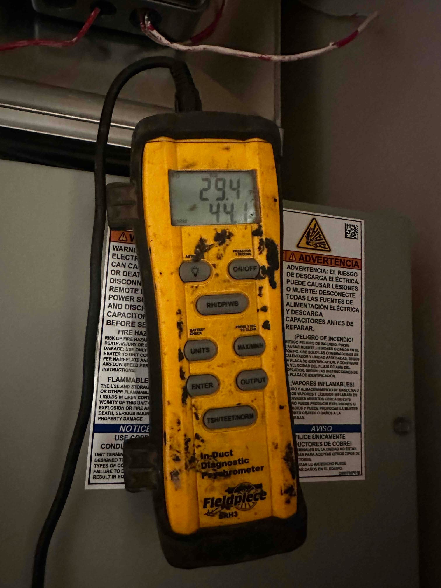 Digital thermometer at the air handler displays two temperature readings during airflow diagnostics in the duct system.